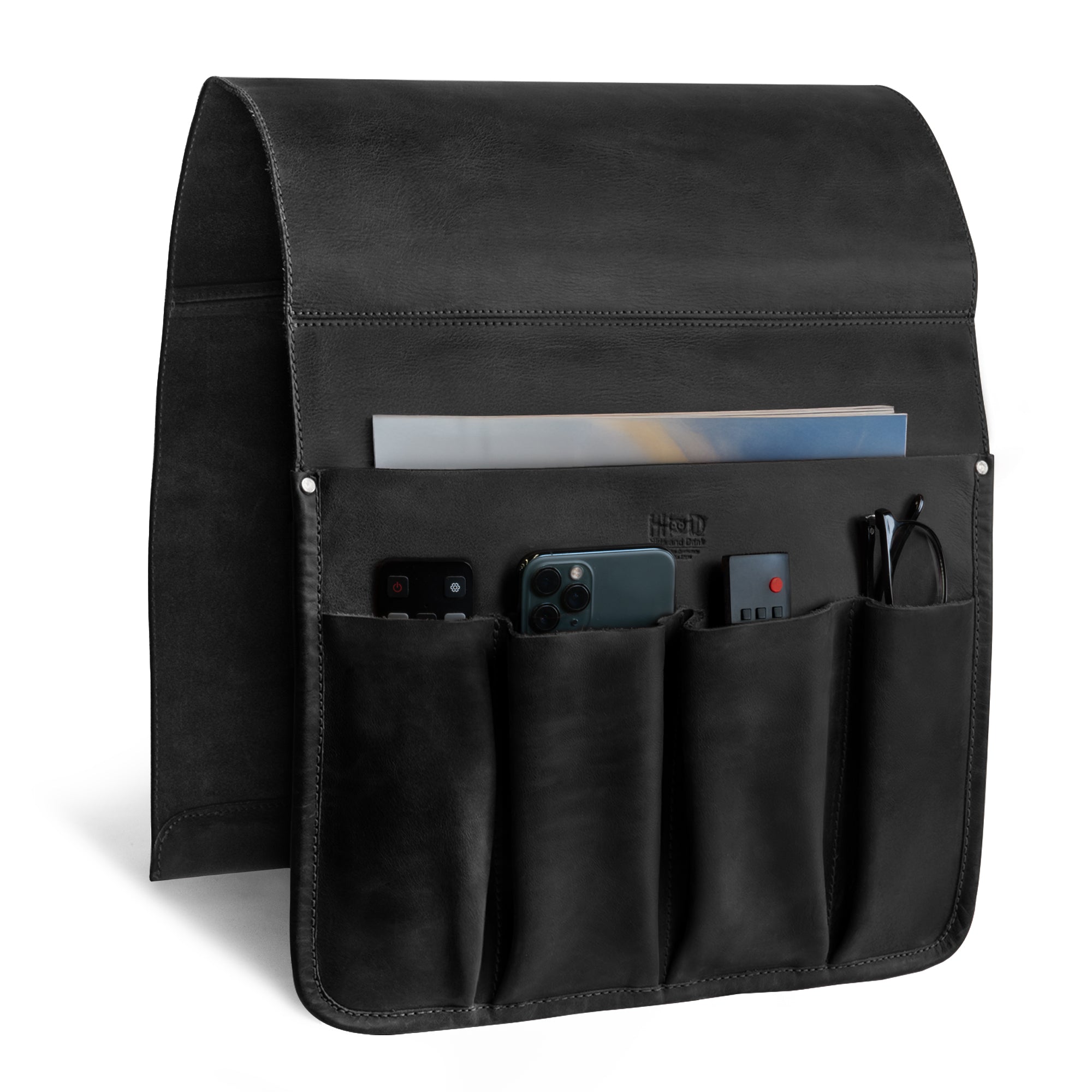 The side view of Hide & Drink’s Remote Control Holder in black leather demonstrates its pocket structure designed for efficient organization. This couch potato essential is ideal as an armchair caddy, merging style and functionality.