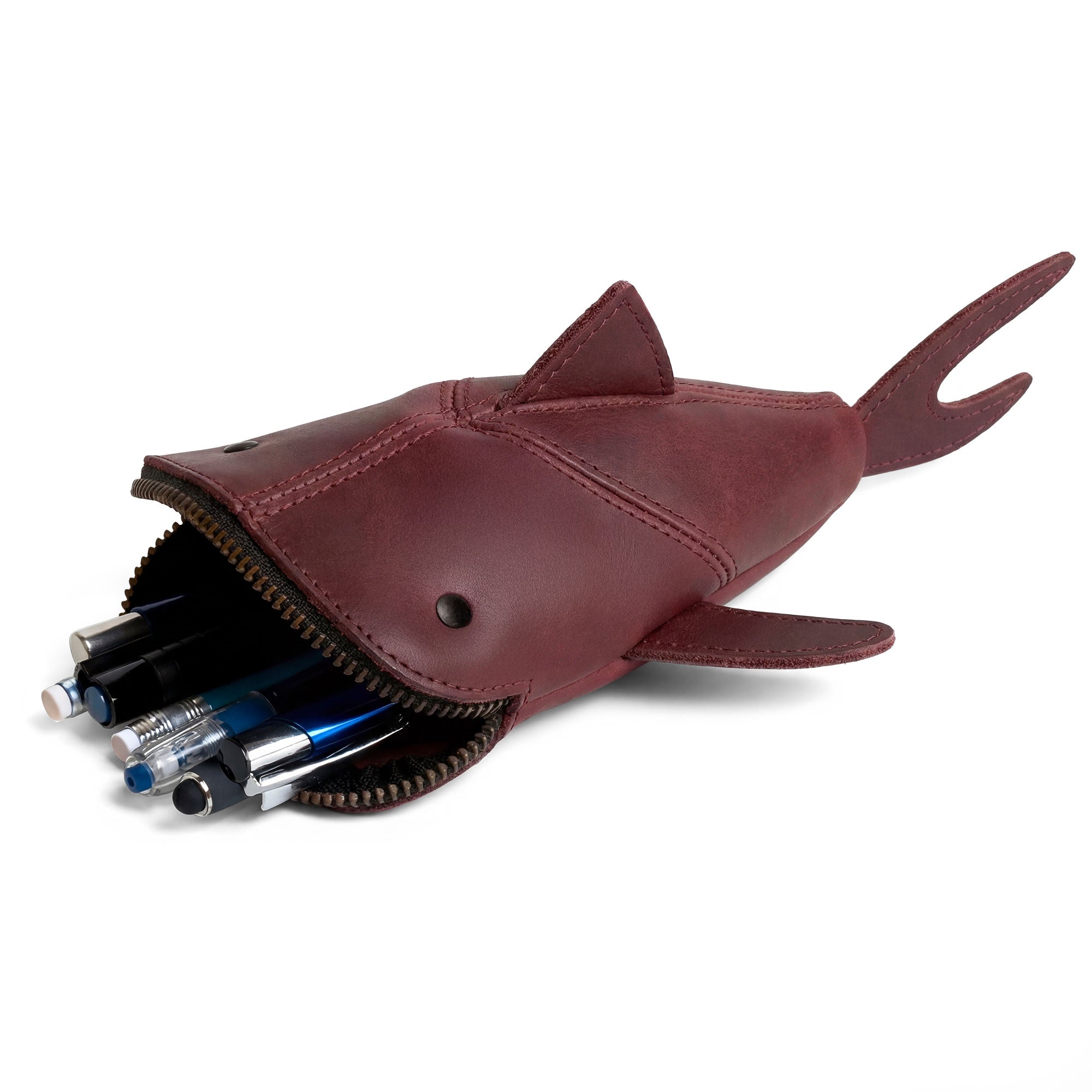 Hide & Drink Leather Shark Pouch filled with pens, showcasing its style and functionality as a zippered coin pouch, change bag, pencil purse, scissors case, and shark-shaped cable holder. Crafted from full grain leather, this artisan-made pouch demonstrates careful hand cut and hand sewn techniques, embodying small batch production from La Antigua Guatemala & Oaxaca Mexico.