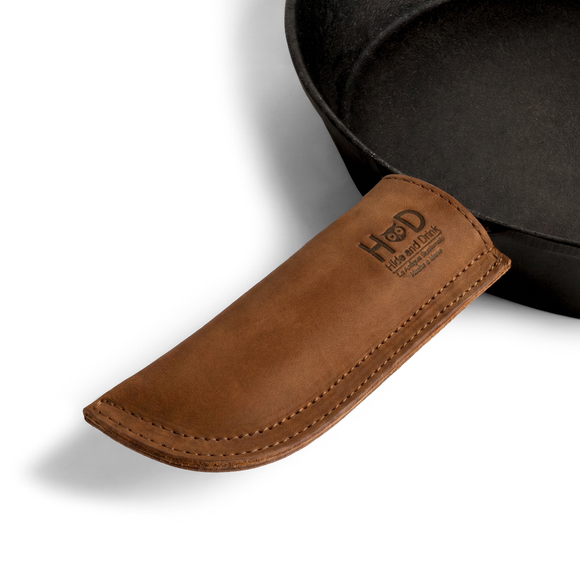 Hide & Drink Cast Iron Panhandle Cover displayed on a metal skillet, showcasing its functionality. This artisan hot handle protector, made from double stitched full grain leather, provides protection while being easy to grip. Handmade in La Antigua Guatemala & Oaxaca Mexico, it’s a perfect blend of style and utility.