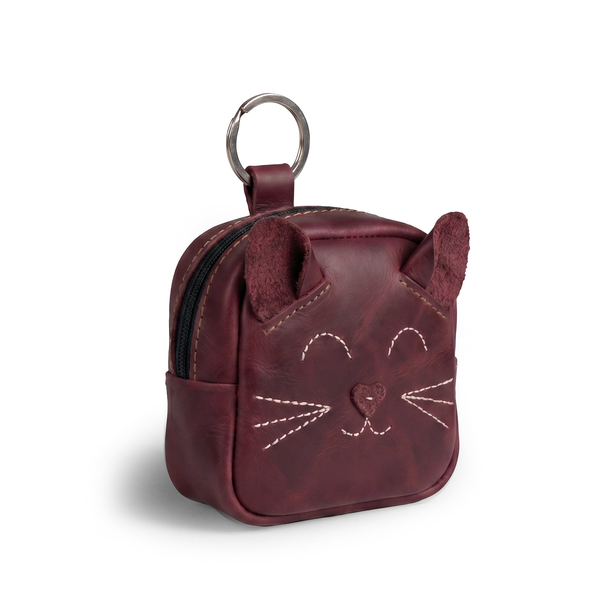 The Cheery Cat Mini Pack from Hide & Drink features a whimsical cat design in rich burgundy, ideal as a coin purse or wallet. This stylish mini backpack is made of Full Grain Leather, showcasing small batch production and artisan craftsmanship from La Antigua Guatemala & Oaxaca, Mexico.