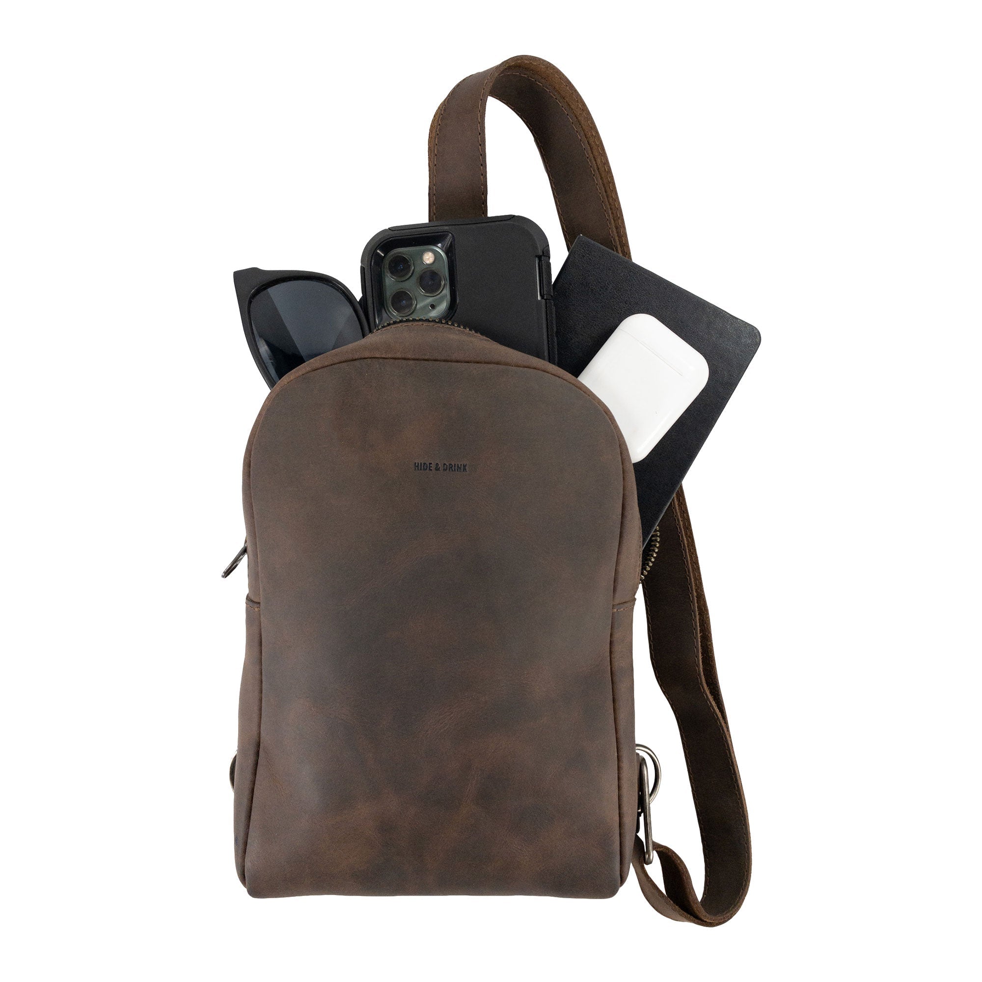 Showcasing the Hide & Drink Crossbody Rounded Bag filled with essentials, this Rounded Crossbody Bag with Adjustable Strap is perfect for travel. Made from Full Grain Leather, it's an artisan piece with small batch production details, hand cut and hand sewn, showcasing the craftsmanship of handmade items from La Antigua Guatemala & Oaxaca Mexico.
