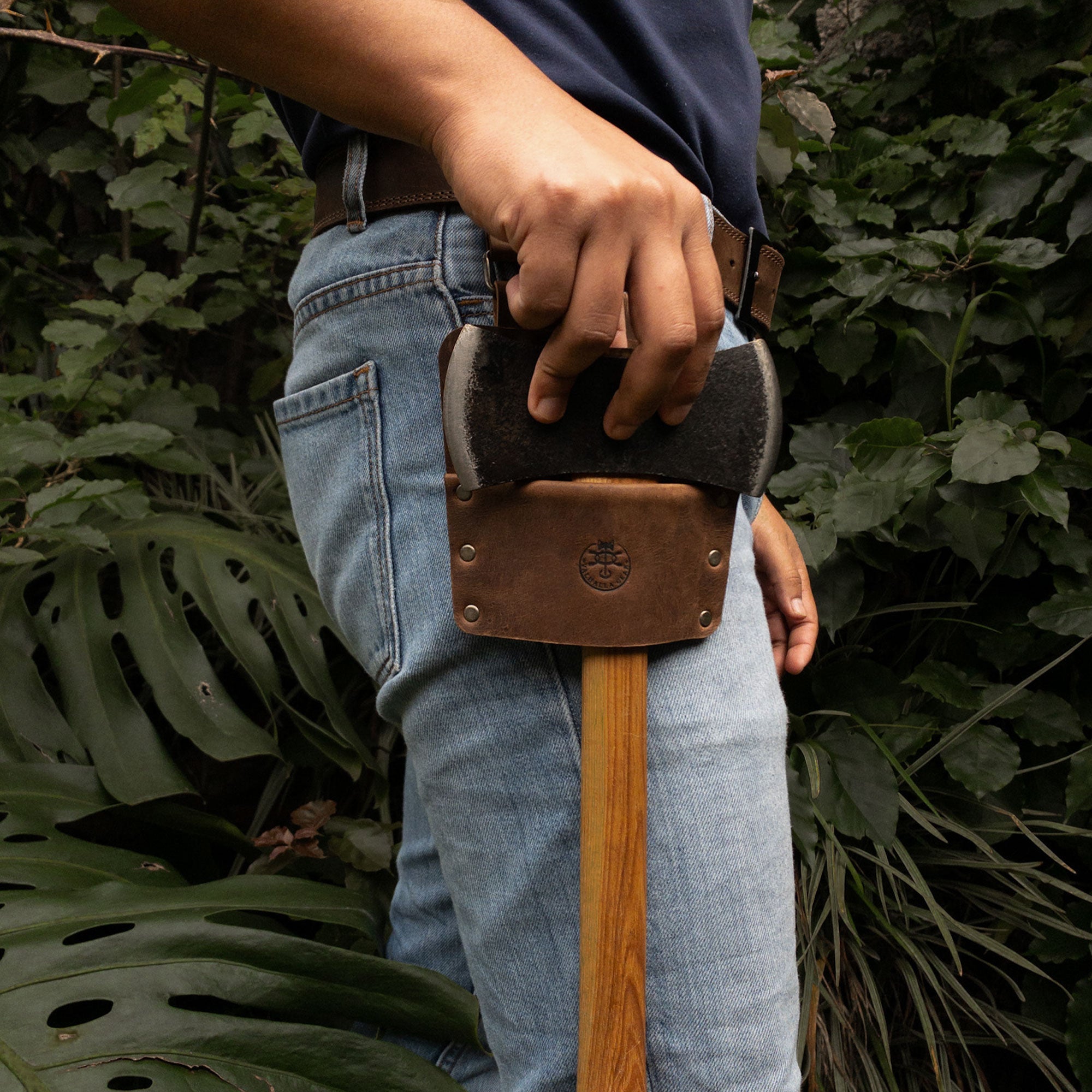 Axe Holster, Durable Carrier for Lumberjack by Valhalla Gear, held by a user in a natural outdoor setting. This full grain leather holster is an ideal accessory for tools, ensuring convenience and safety during home improvement projects. Features artisan craftsmanship from La Antigua Guatemala.