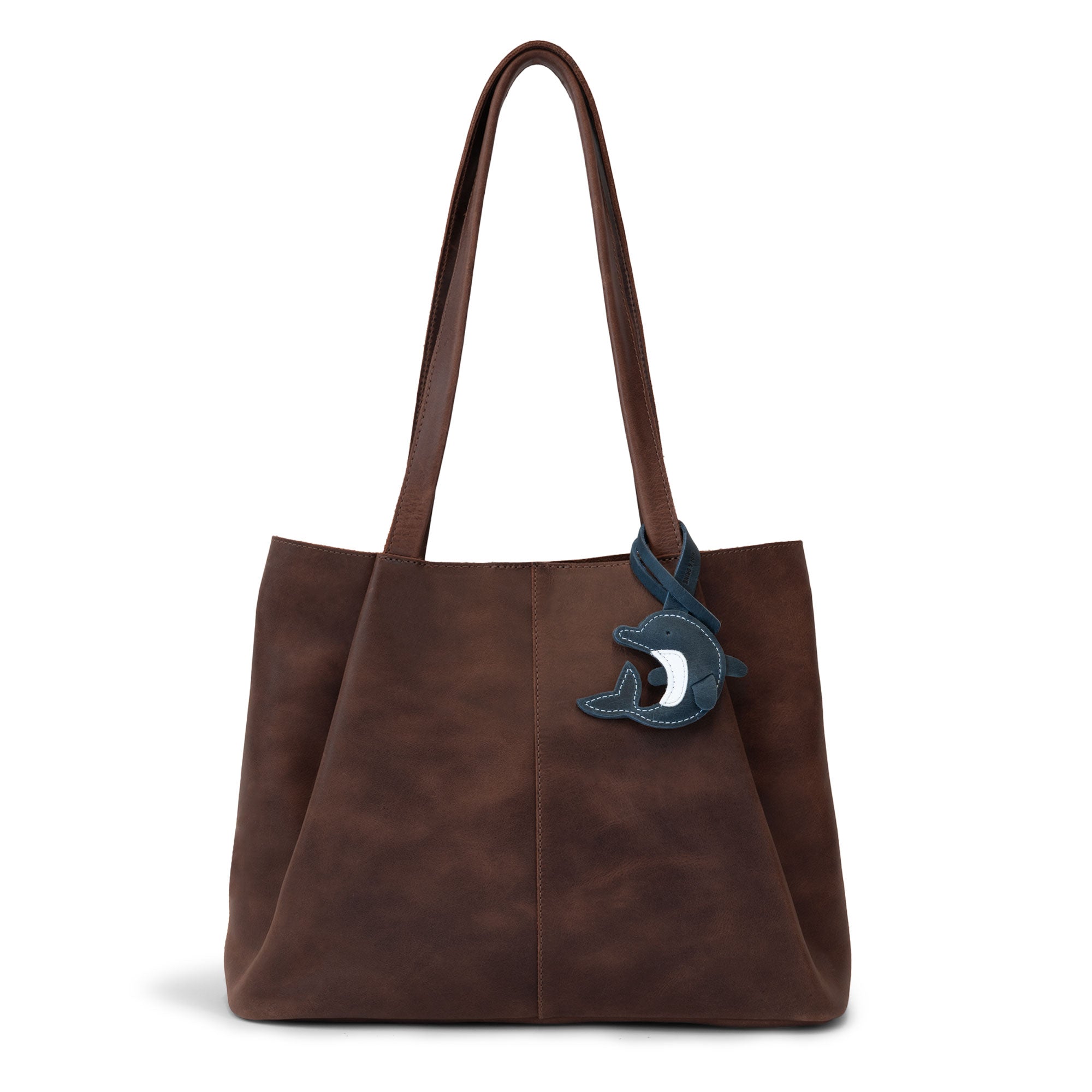 Hide & Drink Bag Charms attached to a trendy brown handbag, showcasing a playful monster design perfect for personalization. This accessory serves as a purse charm for tote & backpacks made from durable full grain leather, highlighting StockyardX's dedication to small batch production. Each piece features hand cut, hand sewn artistry along with fire branding, handmade in La Antigua Guatemala & Oaxaca Mexico.