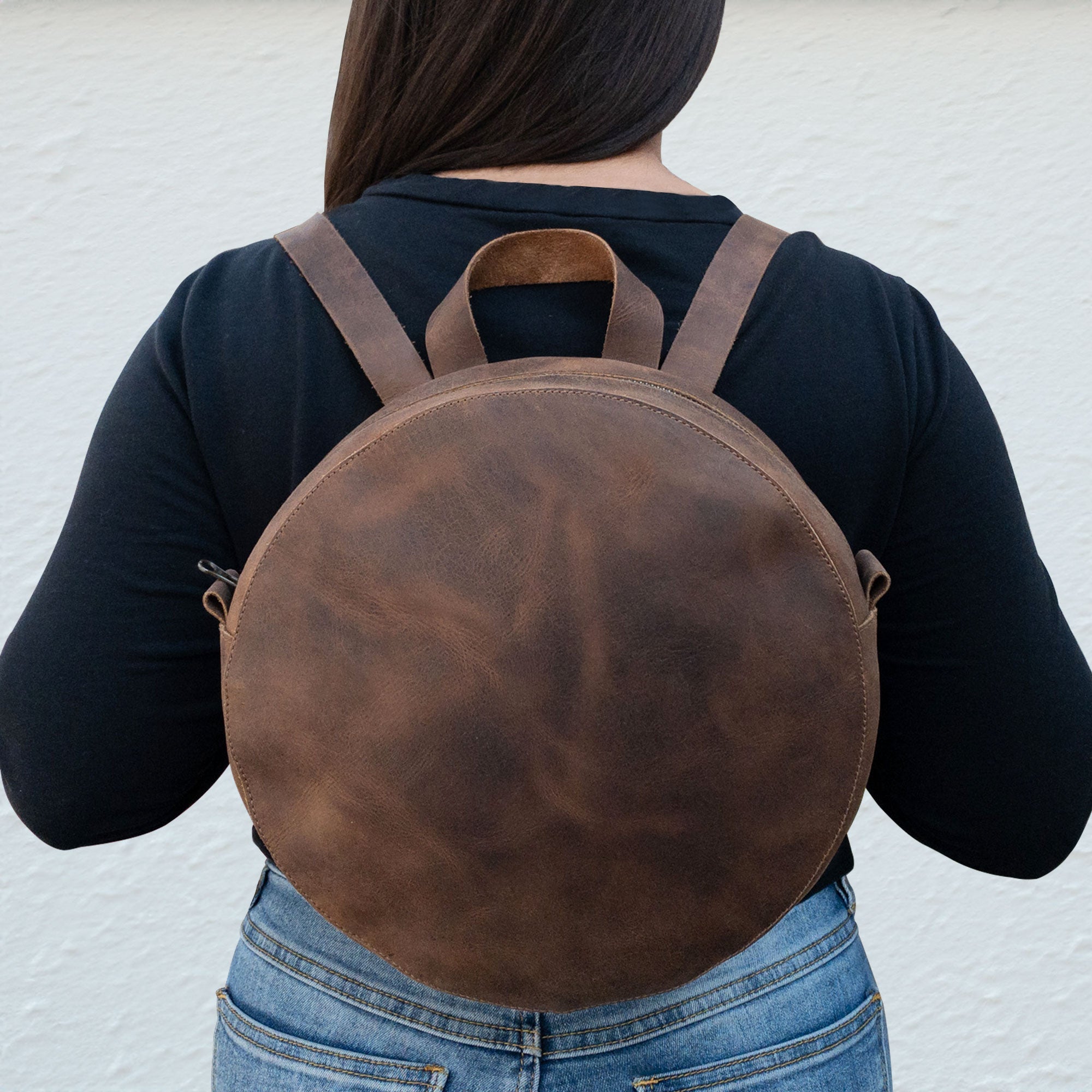 A stylish view of Heather's Circular Backpack worn, displaying its round design in full grain leather. This versatile travel accessory seamlessly transitions into a casual daypack, made with adjustable straps and highlighting the handmade quality by artisans in La Antigua Guatemala & Oaxaca Mexico.