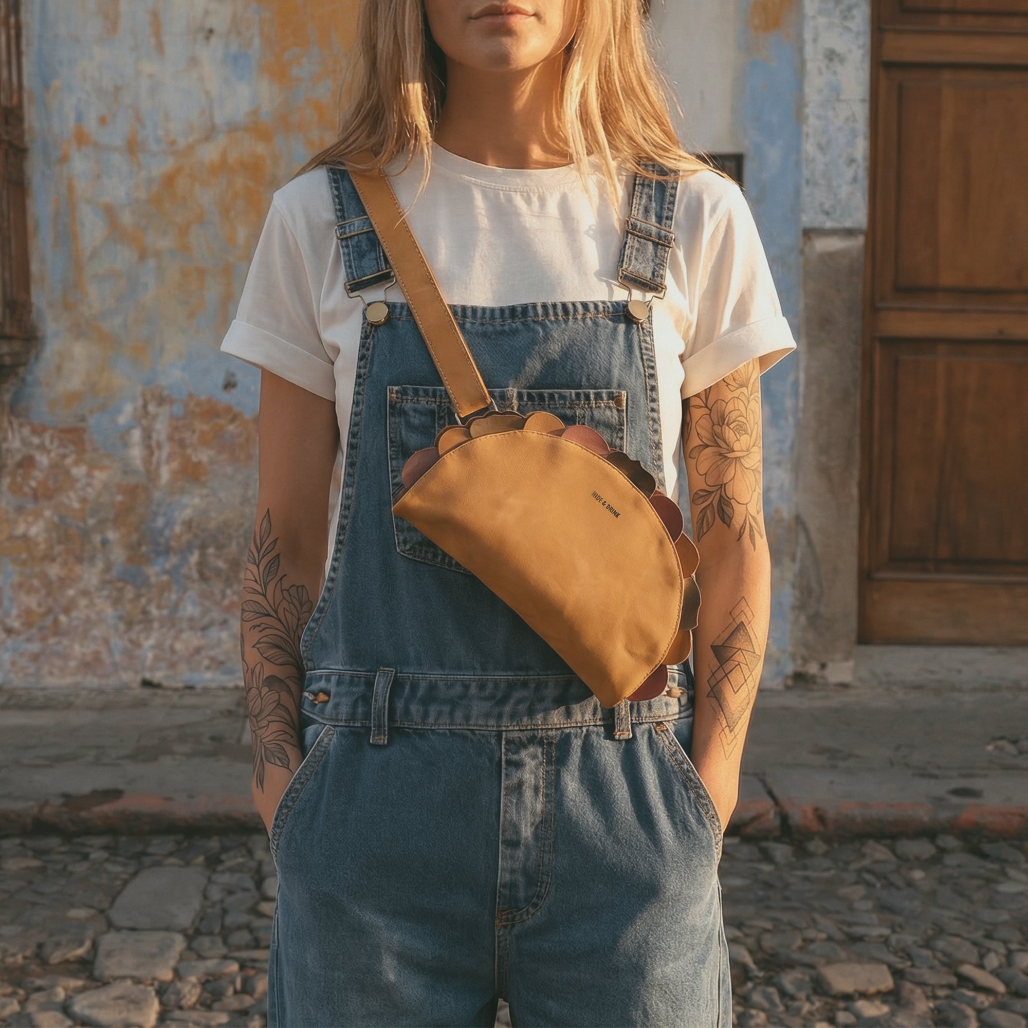 Urban lifestyle shot featuring a woman wearing the Taco-Shaped Crossbody Bag by Hide & Drink. This Leather Taco-Shaped Crossbody Bag with Adjustable Shoulder Strap combines fashion and functionality as a messenger bag that's perfect for day outings. It's crafted from full grain leather through artisan techniques, emphasizing small batch production standards.