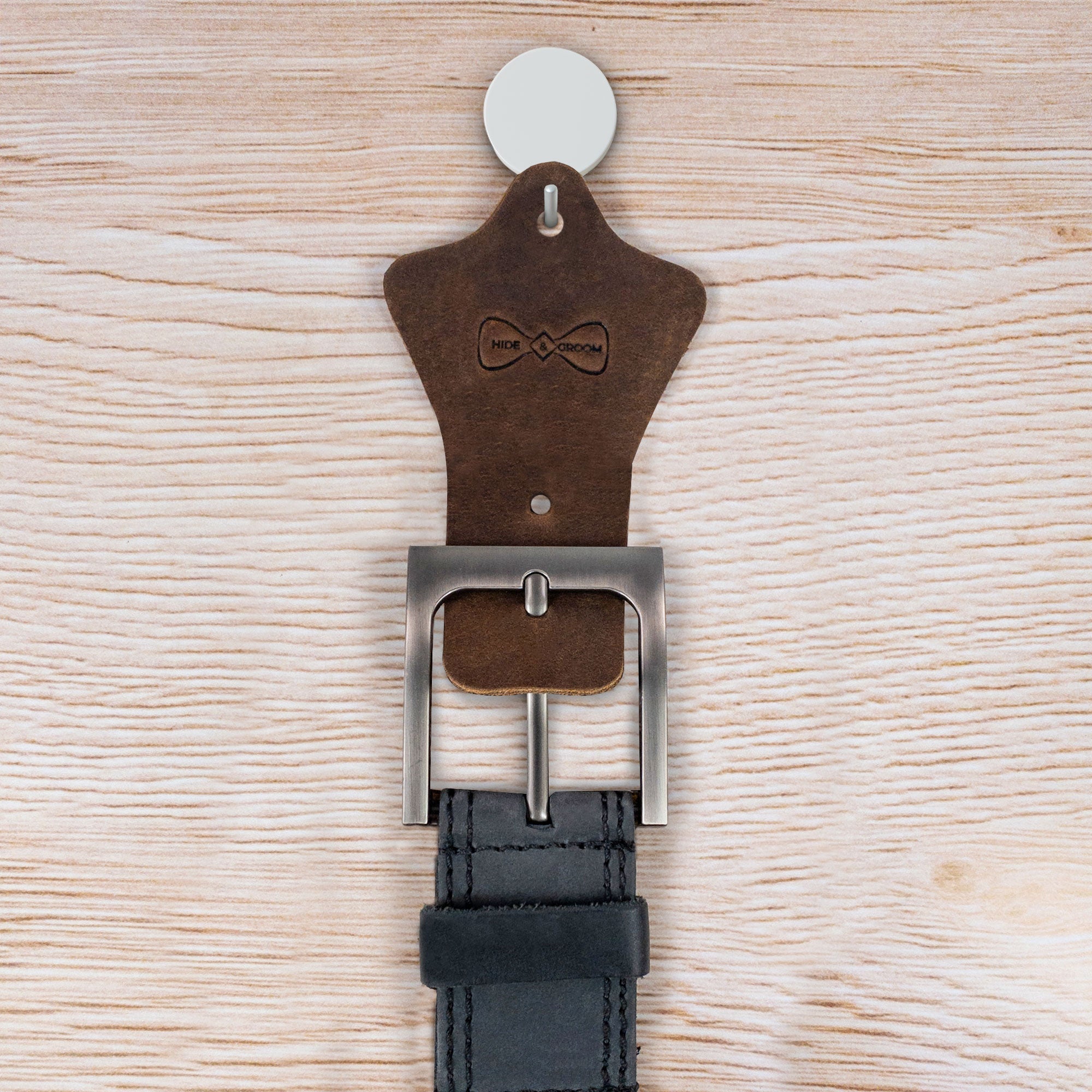 Hide & Groom Set of 2 Buckle Belt Hangers featuring a belt secured in place, ideal for wall mounting to organize your space. Made from high-quality full grain leather, these accessories are a great gift for groomsmen or best man. Crafted in La Antigua Guatemala, this handmade piece supports artisan craftsmanship.
