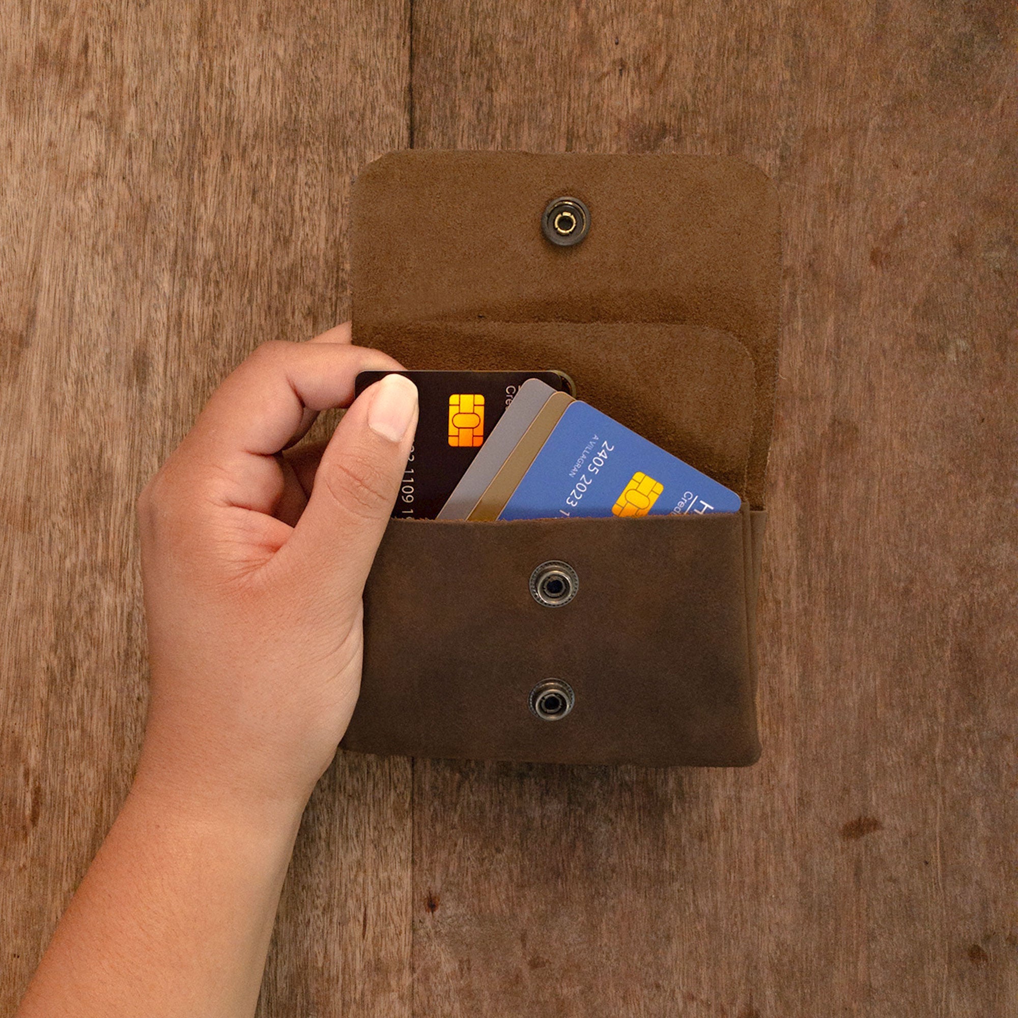 A hand holding the Double Pouch Card Wallet by Hide & Drink, demonstrating its use for storing cards. This Leather Double Pouch Card Wallet is a great choice for anyone needing a card organizer, cash holder, or coin pouch, designed for both men and women. Full Grain Leather, handcrafted in La Antigua Guatemala & Oaxaca Mexico.