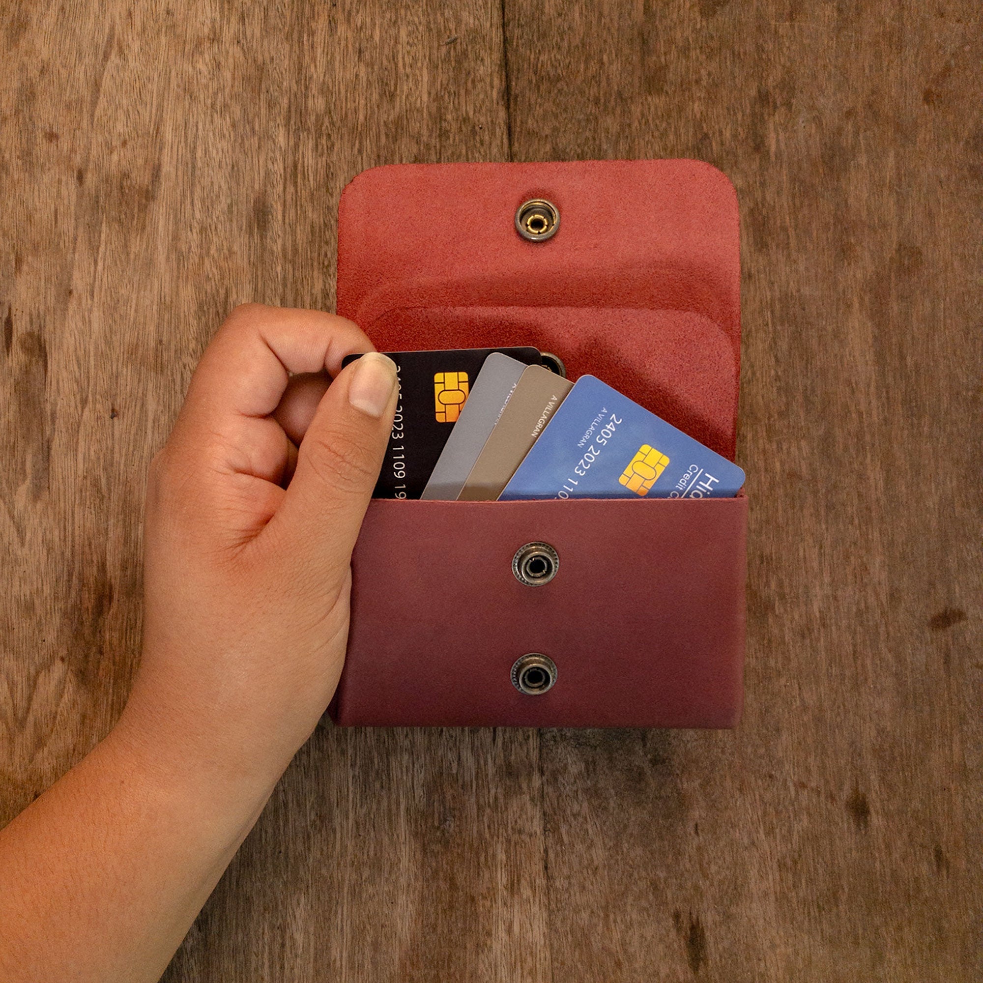 A hand retrieving cards from the burgundy Double Pouch Card Wallet by Hide & Drink. This Leather Double Pouch Card Wallet is functional as a card organizer, cash holder, or coin pouch, perfect for men and women, crafted from Full Grain Leather in La Antigua Guatemala & Oaxaca Mexico.