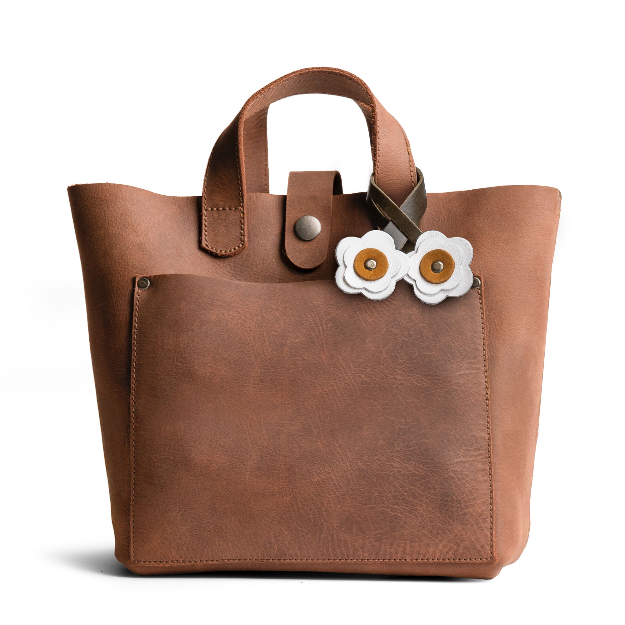 Elegant view of the white flower-shaped Rose Bag Ornament by Hide & Drink on a bag, illustrating its Full Grain Leather quality. A charming accessory for totes, perfect for a stylish touch.