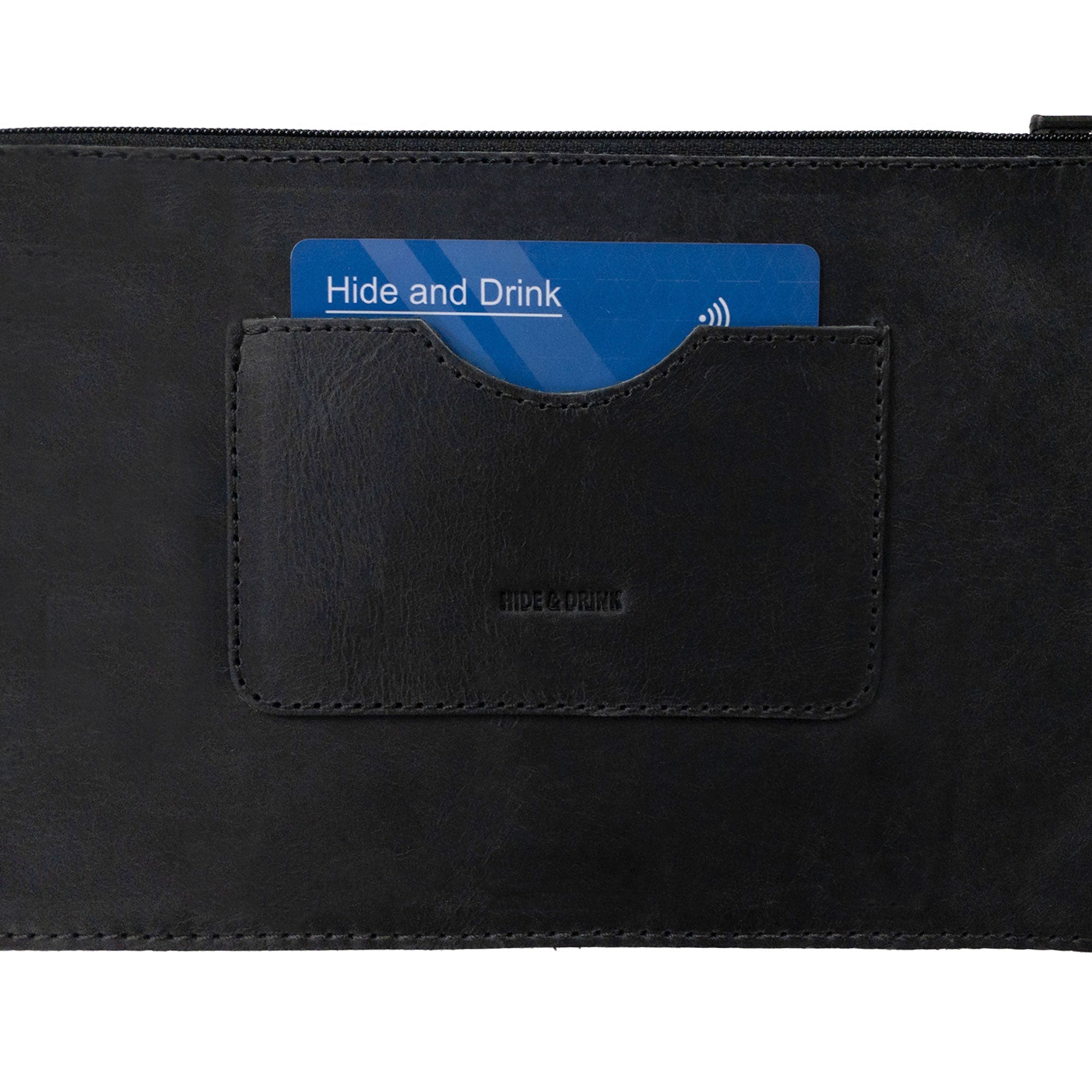 Close-up view of a black rectangular zippered handbag by Hide & Drink, emphasizing the card slot. This female purse is crafted from durable full grain leather, ensuring quality. Highlighting artisan craftsmanship, it is handmade with care in small batch production, made in La Antigua Guatemala & Oaxaca Mexico.