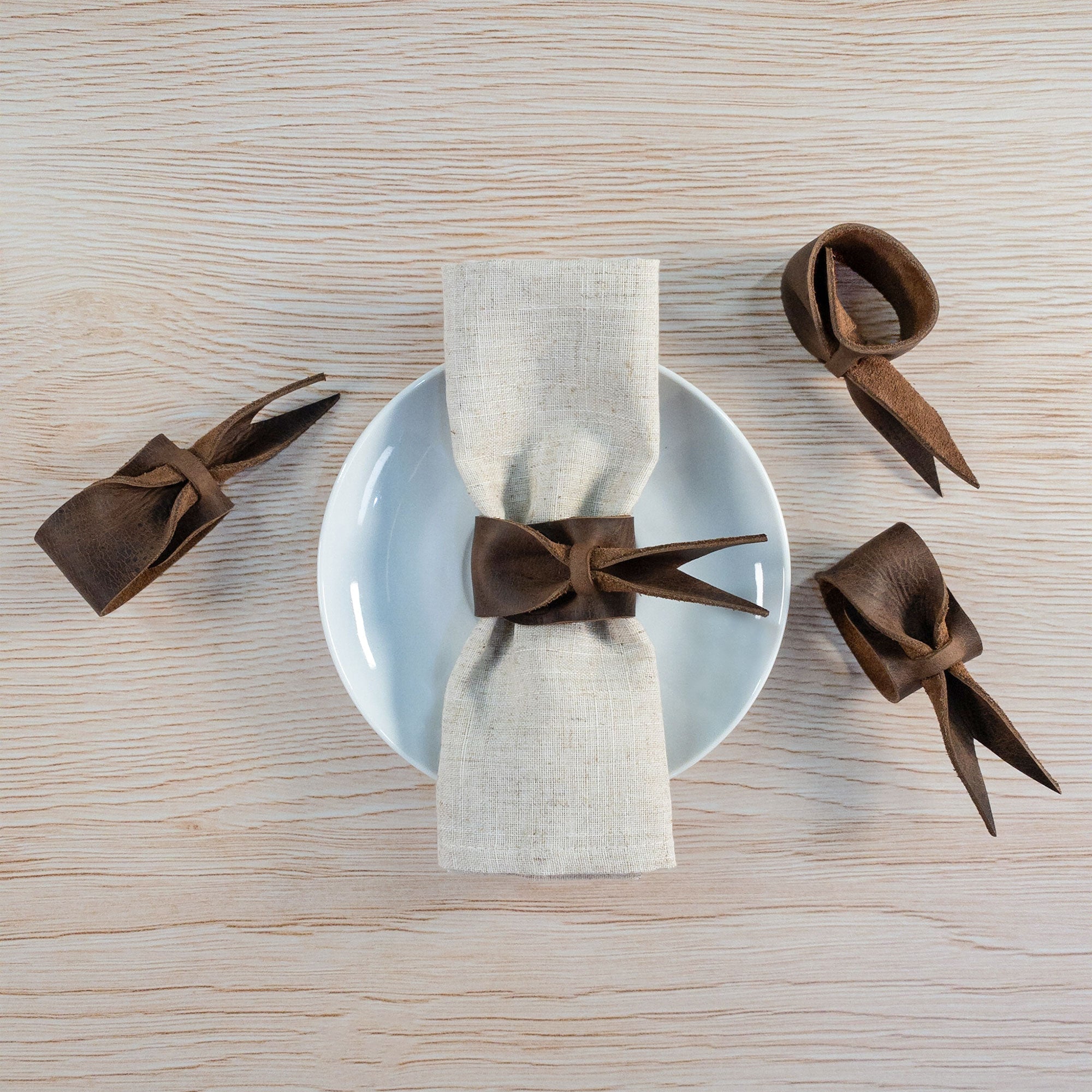 Stylish Set of 4 Napkin Rings for Weddings by Hide & Groom, featuring leather napkin rings styled with bows on a plate setting. Ideal for dinner parties and wedding decorations, made from full grain leather, highlighting artisan craftsmanship from small batch production in La Antigua Guatemala & Oaxaca Mexico.