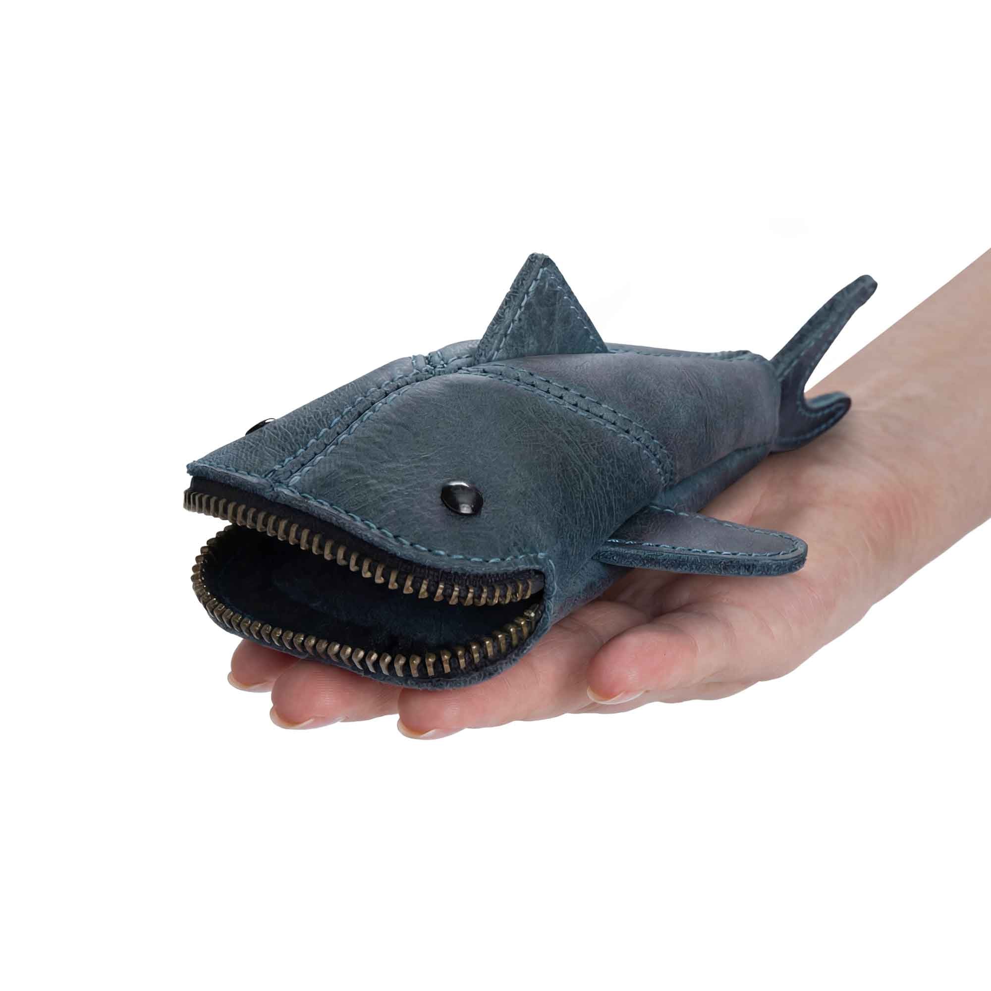Hide & Drink Leather Shark Pouch displayed in a hand to show size. This leather pouch, shaped like a small shark, serves as a stylish Leather Coin Purse and small charger cable holder. Its design makes it an excellent change bag or zippered cable case, perfect for keeping cash organized. Made from high-quality full grain leather, this product is part of the small batch production process, hand cut, hand sewn, and fire branded by artisans in La Antigua Guatemala & Oaxaca Mexico.