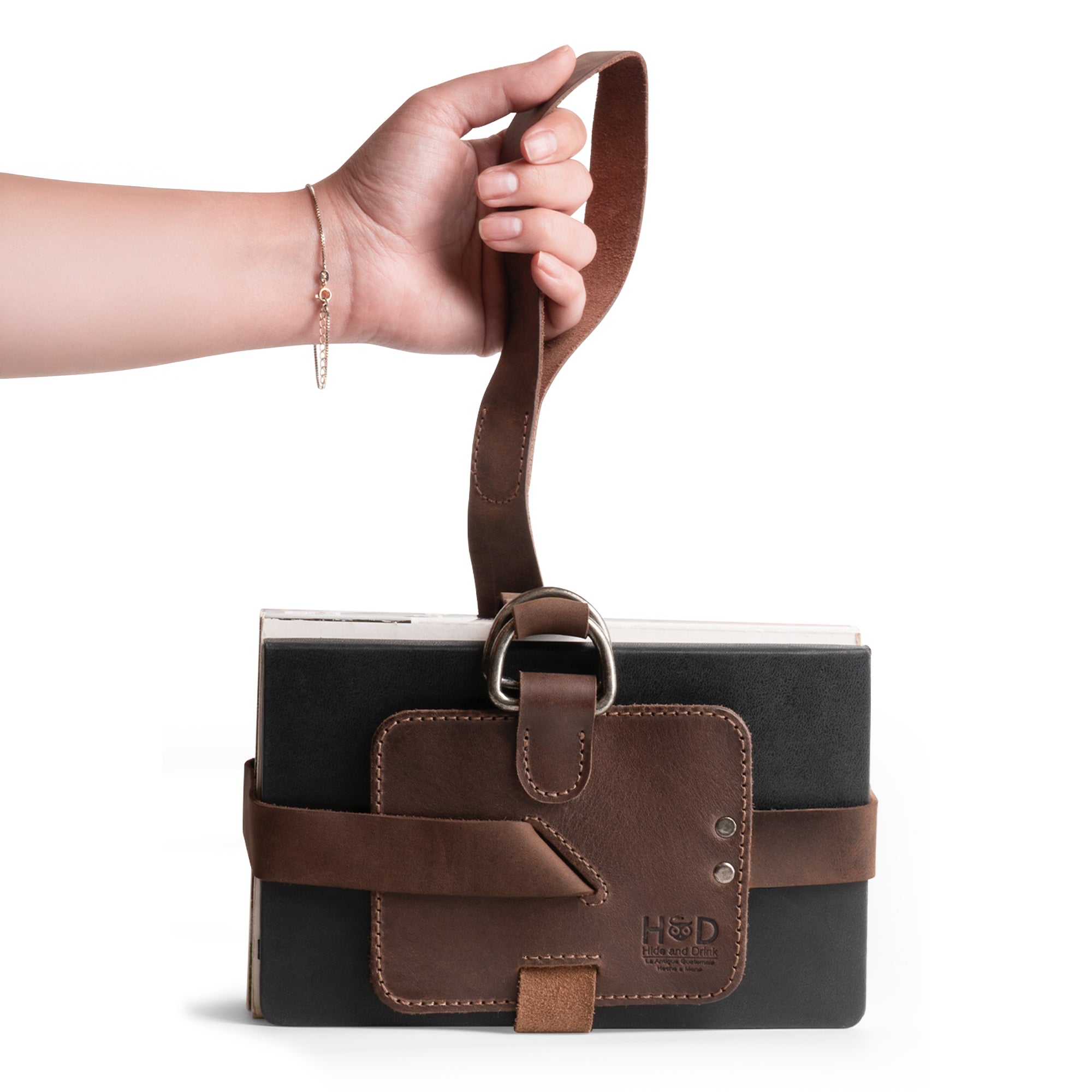 A hand modeling the Hide & Drink Book Strap Carrier, highlighting its ergonomic design and comfortable shoulder carry feature. Perfect for carrying books, this Full Grain Leather carrier is handmade in La Antigua Guatemala, blending style and function.