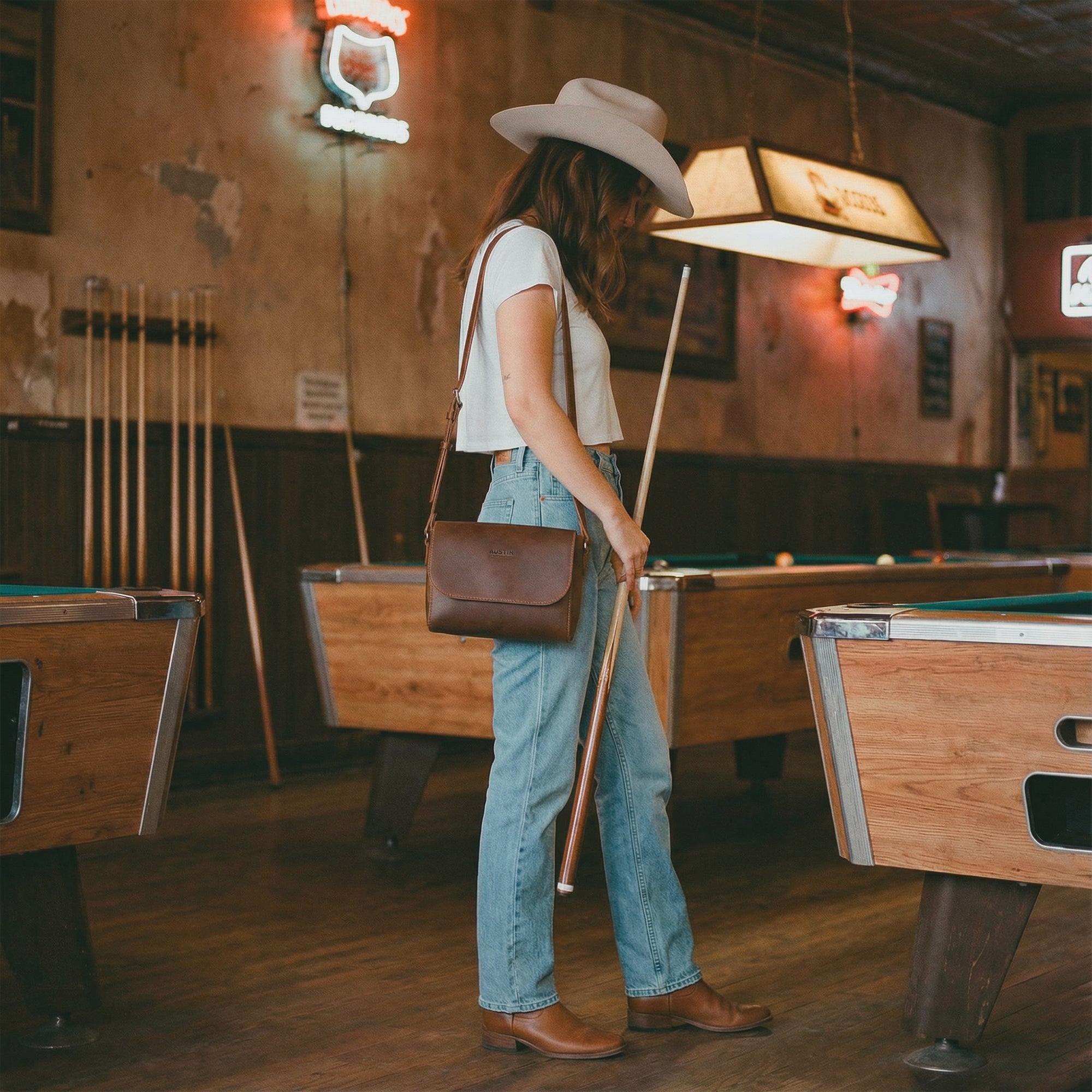 The Barton Purse by Austin Genuine is shown in a casual setting, worn stylishly with a hat, embodying the free spirit of Texas culture. Made from full grain leather and handcrafted in small batches, it reflects the artisan quality of being hand cut and sewn, inspired by the vibrant popular culture of Austin.