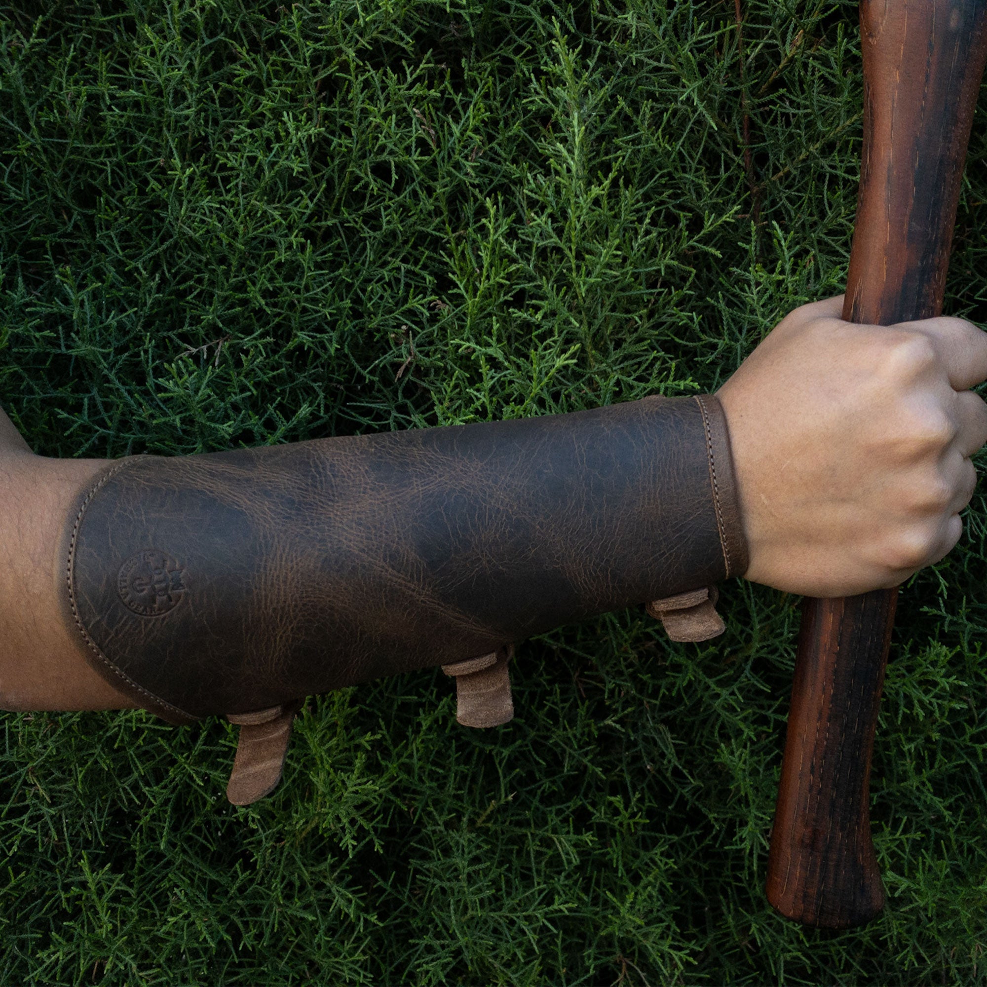 A model wearing the Rustic Archery Bracer by Valhalla Gear, demonstrating its versatility as a forearm protector for knights. Made from full grain leather and featuring adjustable buckle straps, this handmade piece is ideal for cosplay. Artisan craftsmanship highlights the small batch production from La Antigua Guatemala & Oaxaca Mexico.