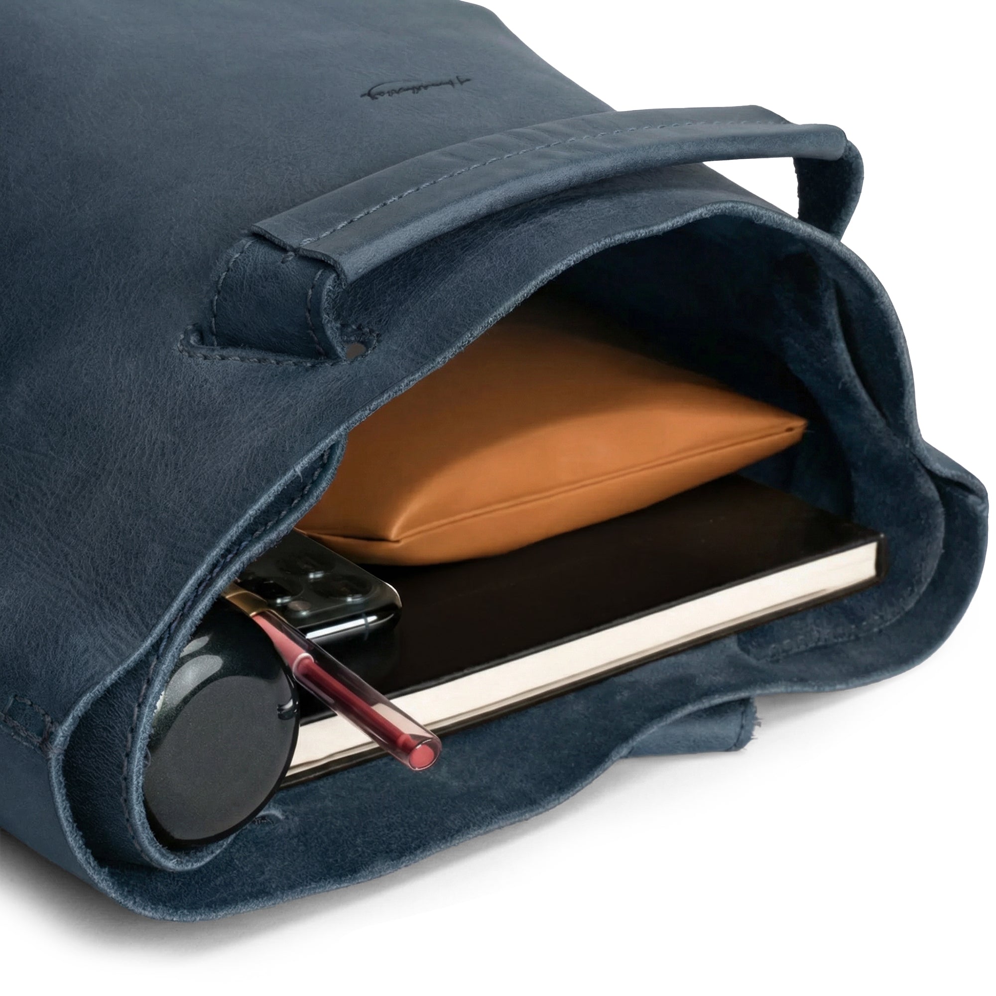 Interior view of Heather's Convertible Backpack to Shoulder Bag, filled with everyday essentials like notebooks and a device. This spacious crossbody for women made from Full Grain Leather embraces small batch production and artisan techniques, handmade in La Antigua Guatemala & Oaxaca Mexico.