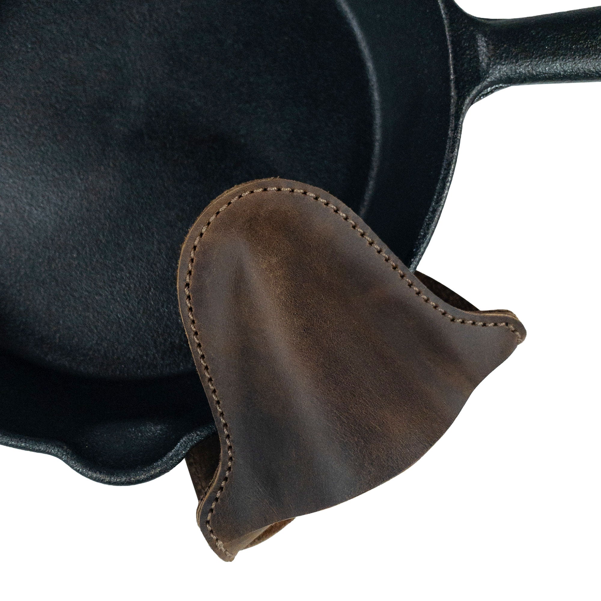 The Oven Mitt Heat Resistant from Cast Leather Co. gracefully resting on a cast iron pan, demonstrating its heat protection features. This oven glove is made from full grain leather and is an essential rustic potholder for kitchen cooking and baking. Proudly handmade in La Antigua Guatemala with small batch production techniques.