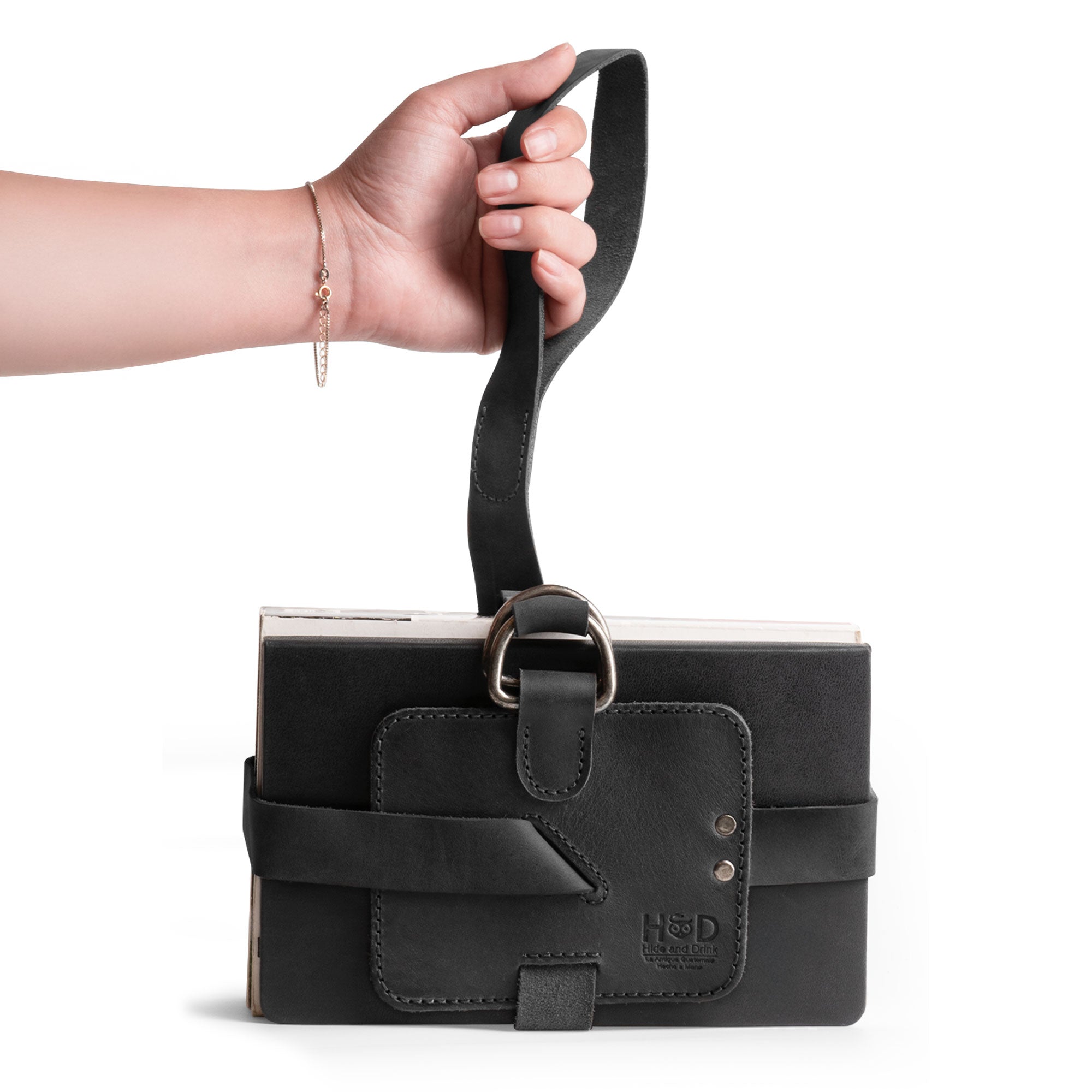 A person carrying a stylish Hide & Drink Book Strap Carrier using the shoulder strap, showcasing its functional design. Made of Full Grain Leather, this artisan product is handcrafted in La Antigua Guatemala for avid readers.