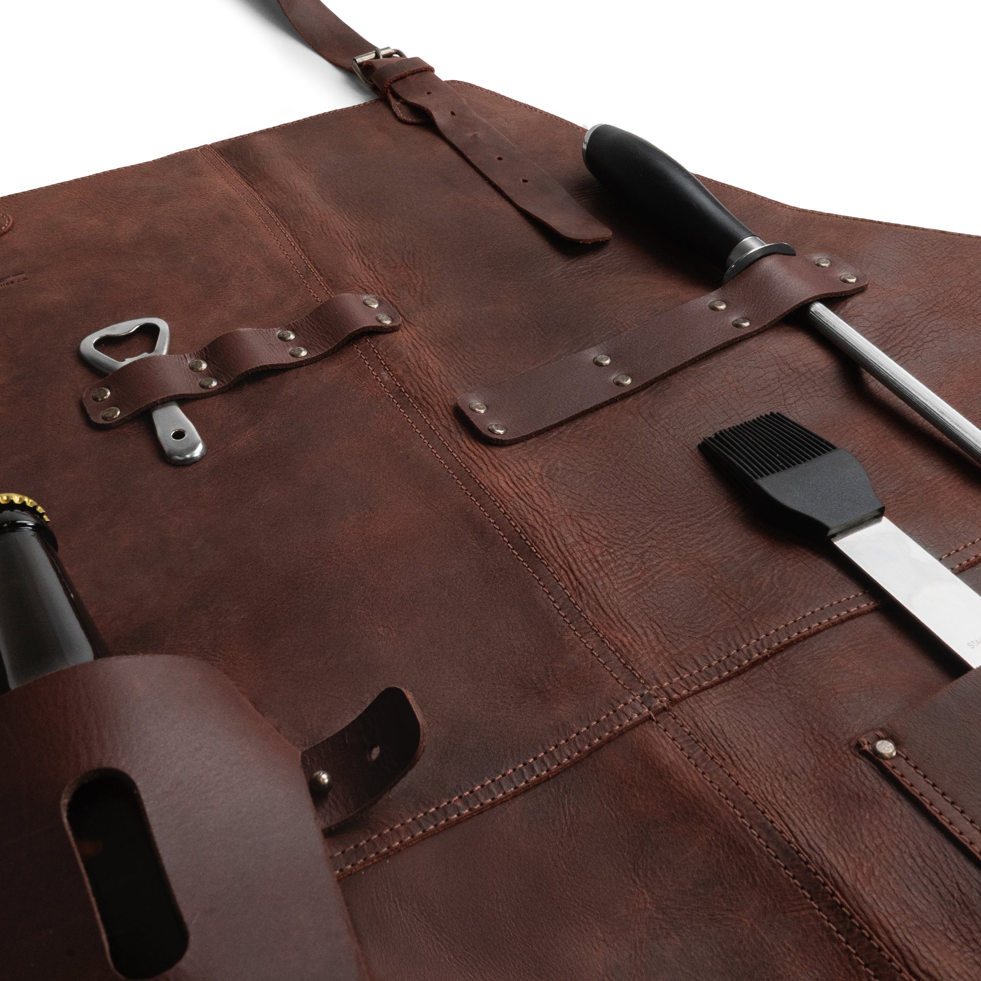 Detailed view of Cast Leather Co. BBQ Apron, showcasing pockets and tools, emphasizing its rustic charm. Made from full grain leather, this artisan BBQ Apron is designed for cooking with convenience, exemplifying small batch, hand cut, and hand sewn production.