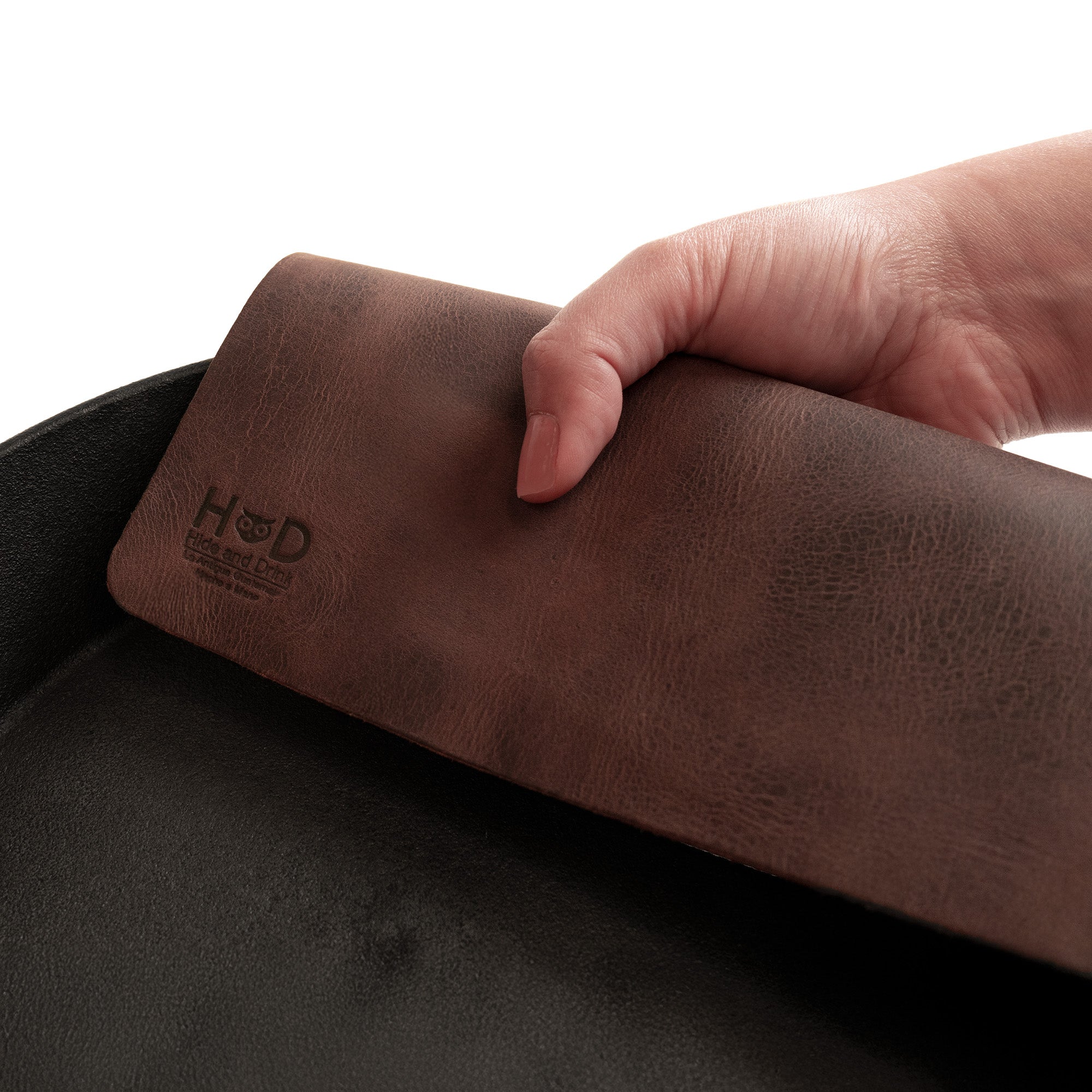 Close-up of Hide & Drink's Potholder Sheet being used to handle a hot skillet, highlighting its functionality and design. This full grain leather protection sheet is a must-have for cookware, showcasing handmade quality and artisan craftsmanship from La Antigua Guatemala & Oaxaca Mexico. The Squared Potholder Sheet is a staple in any kitchen.