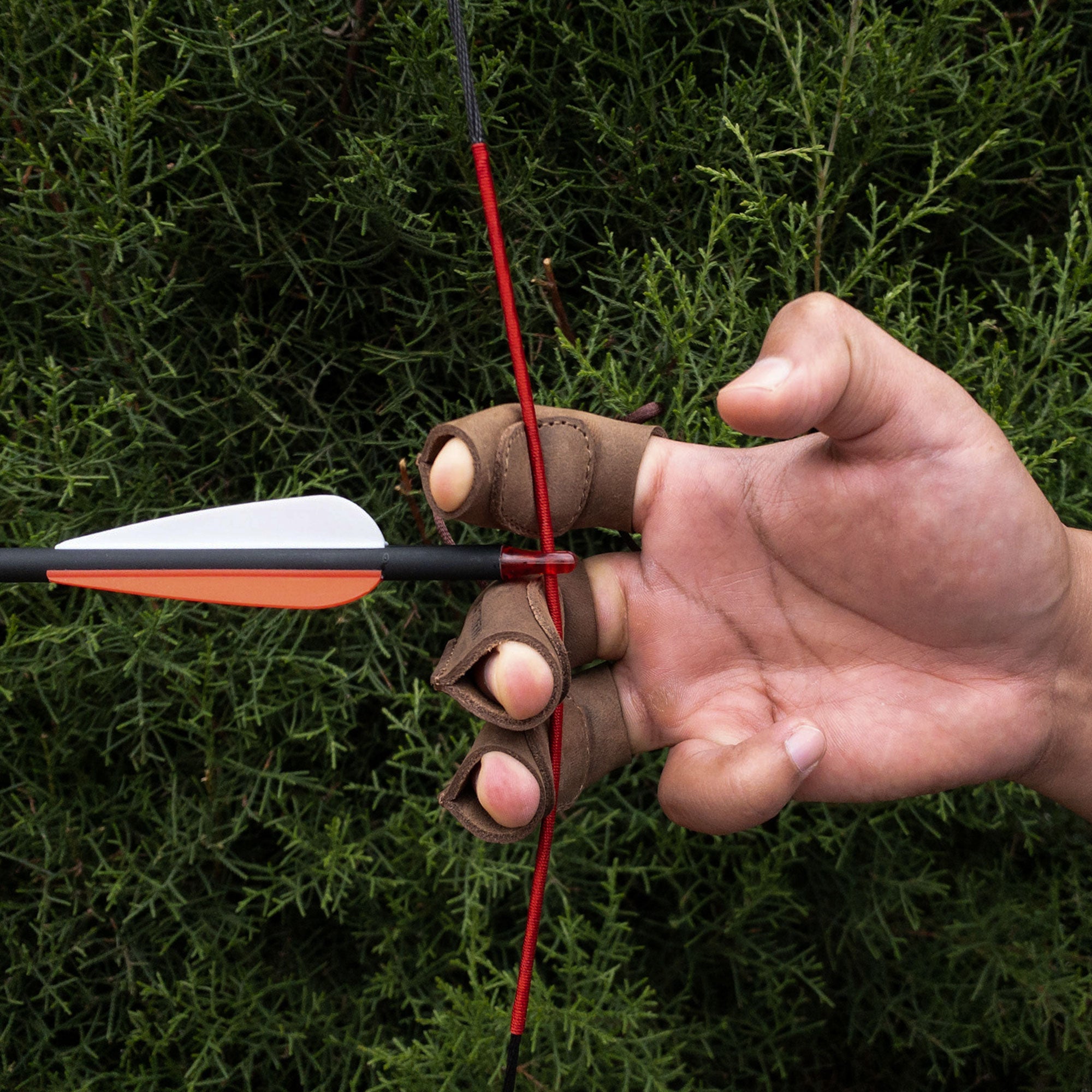 An archer's hand gripping an arrow while wearing the Set of 3 Finger Protectors for Archery by Valhalla Gear. This hand guard is crafted from durable full grain leather, making it an essential piece of archer accessories for recurve bows and shooting targeting. It showcases artisan craftsmanship with small batch production and fire branded details, handmade in La Antigua Guatemala.