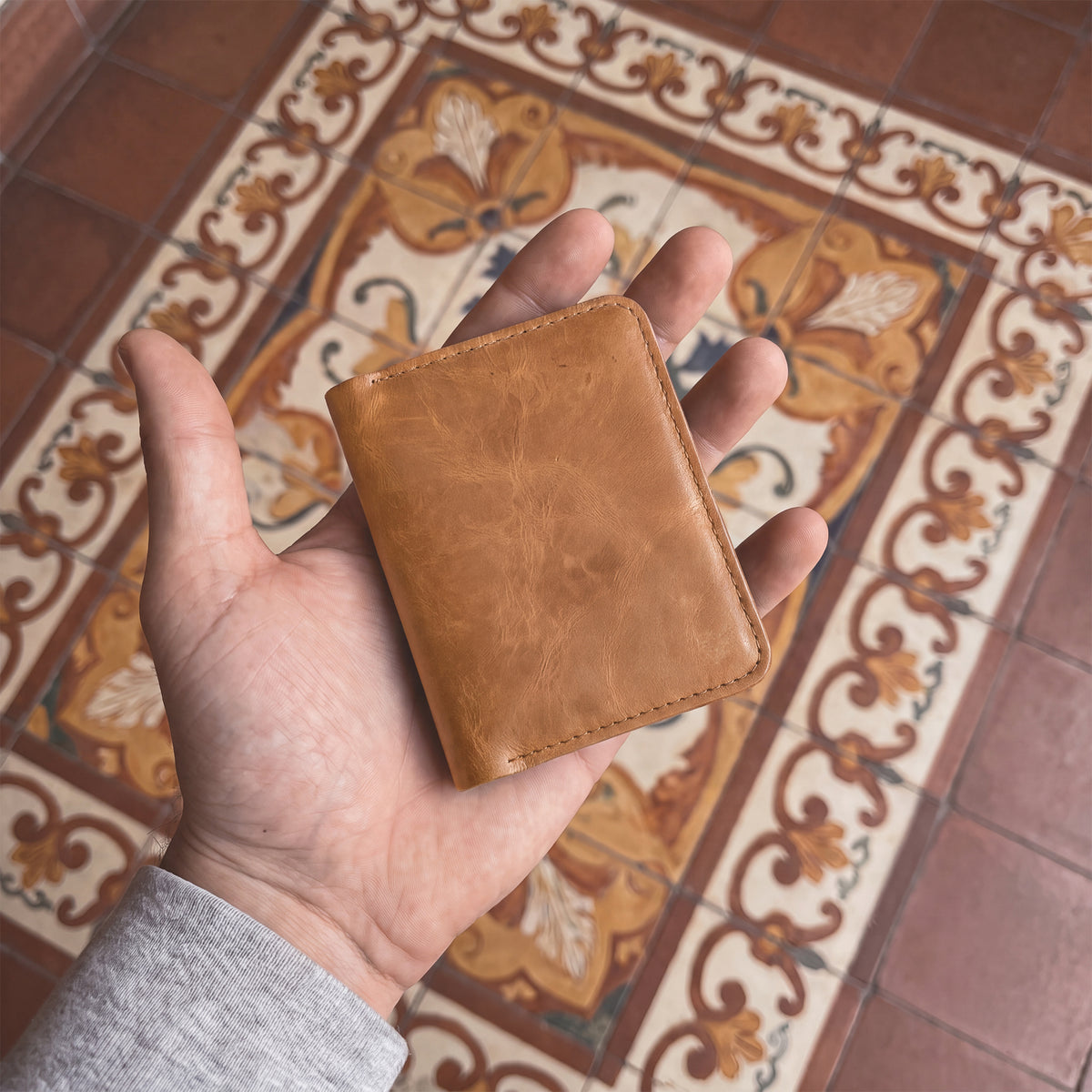 A held brown Bi-Fold Card Wallet Diagonal by Hide & Drink illustrating its compact design, perfect for organization and made with artisan quality full grain leather.