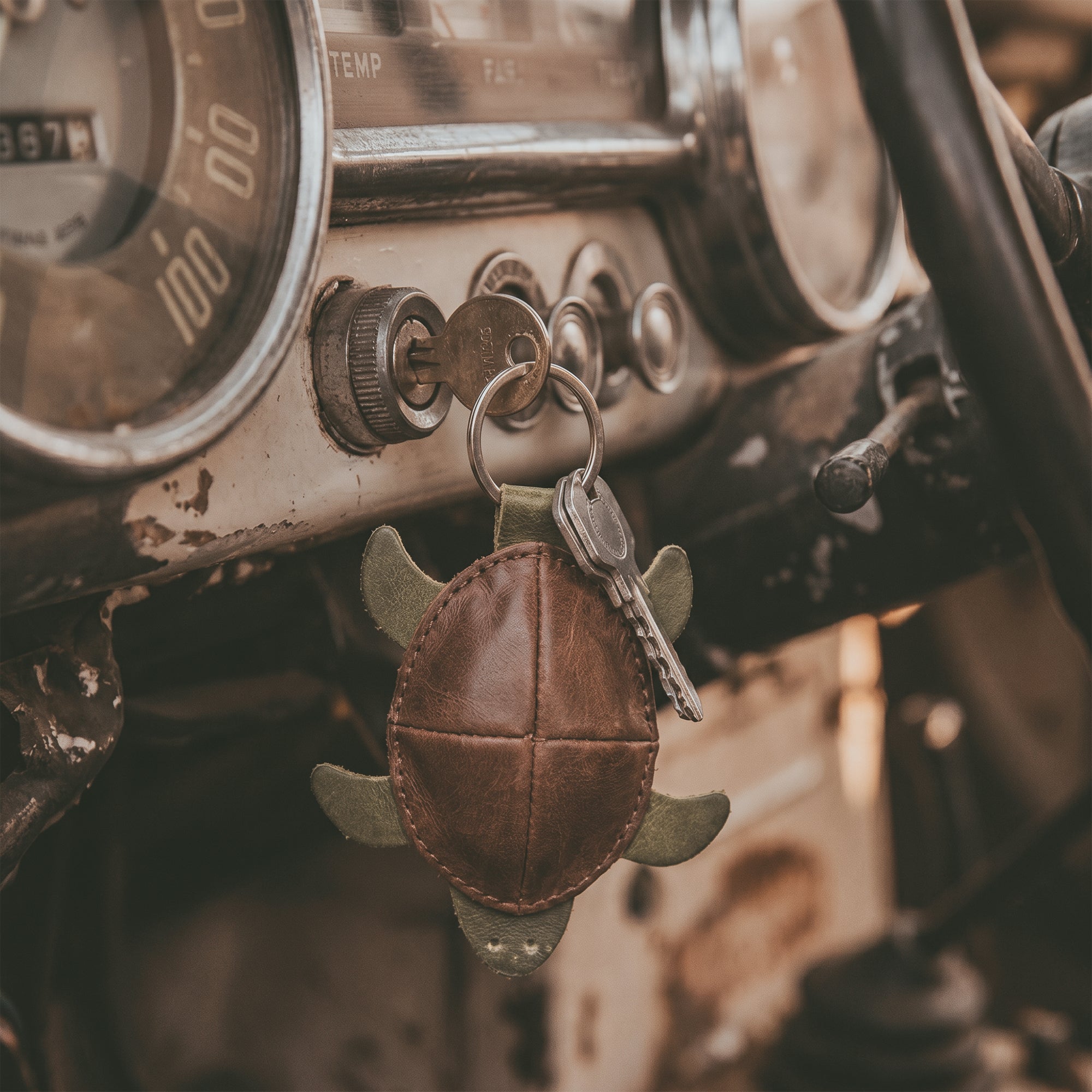 Turtle Mini Pouch Keychain by Hide & Drink, displayed in a vintage car’s ignition area, emphasizing its practical use. This Leather Turtle Coin Purse serves as a unique cable holder and USB organizer, made from Full Grain Leather with artisan craftsmanship from La Antigua Guatemala.