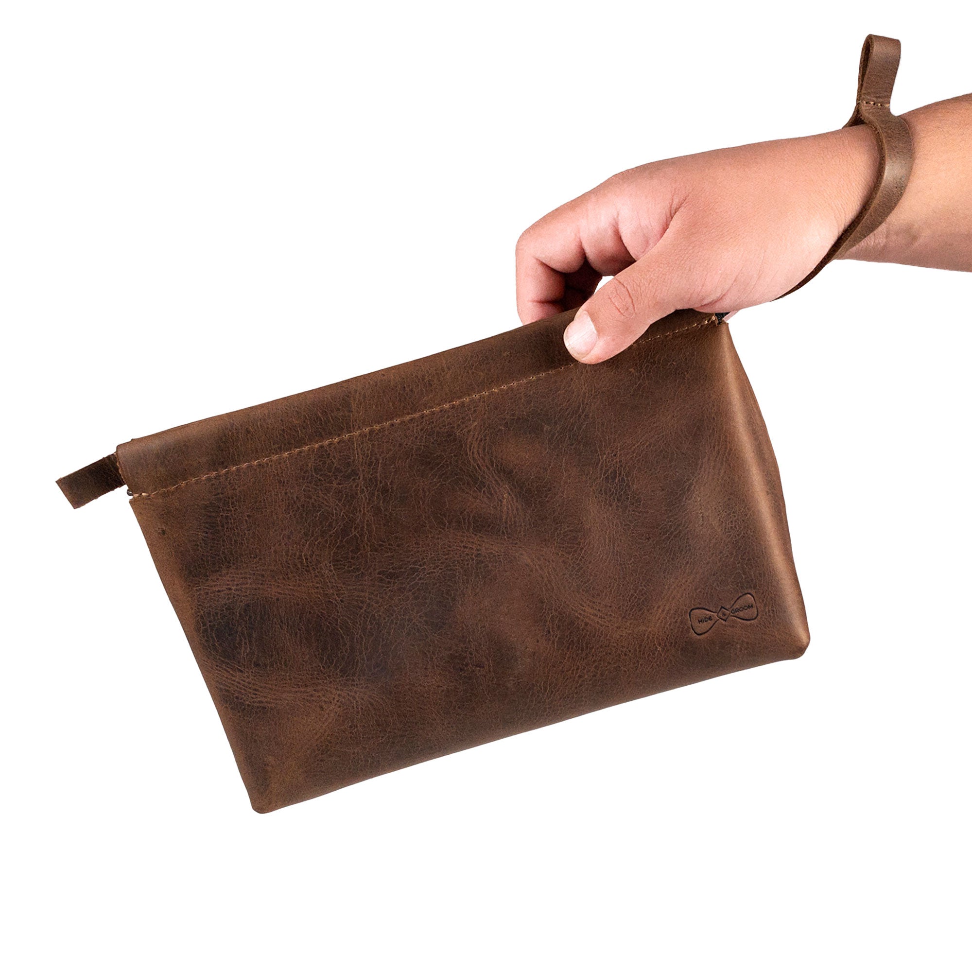 A person holding the Rectangular Toiletry Bag with Sliding Handle for Groomsmen by Hide & Groom, demonstrating its practical size and elegant design. Made from full grain leather, this bag is perfect for groomsmen and acts as a stylish shaving kit storage, exemplifying small batch production.