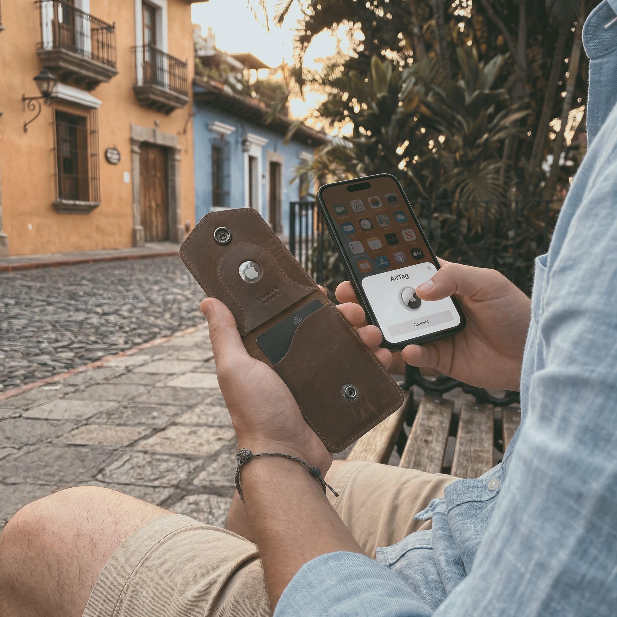 A customer interacts with the Card Holder with AirTag Slot by Hide & Drink while using a smartphone outdoors. This handmade wallet, crafted from full grain leather, functions as a durable storage case for cash and cards, reflecting artisan skills from La Antigua Guatemala and Oaxaca Mexico.