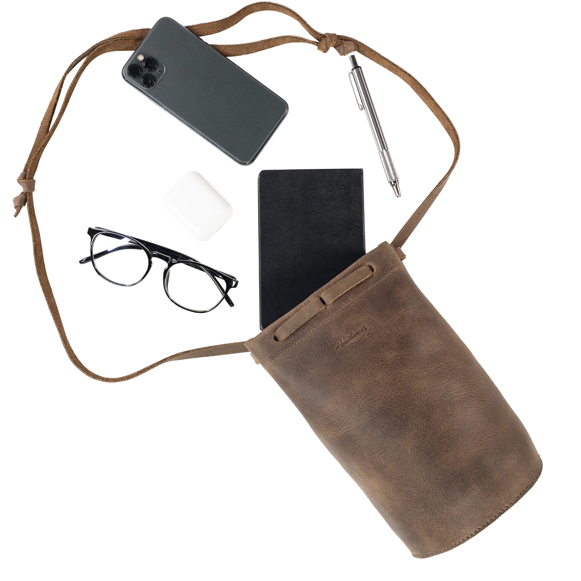 Inside view of Heather's Cylinder Shoulder Phone Bag with essentials laid out, demonstrating its large capacity as a crossbody bag. This cylinder-shaped purse with an adjustable shoulder strap is crafted from full grain leather reflecting artisan craftsmanship from StockyardX, emphasizing small batch production and hand cut, hand sewn quality. Handmade in La Antigua Guatemala & Oaxaca Mexico.