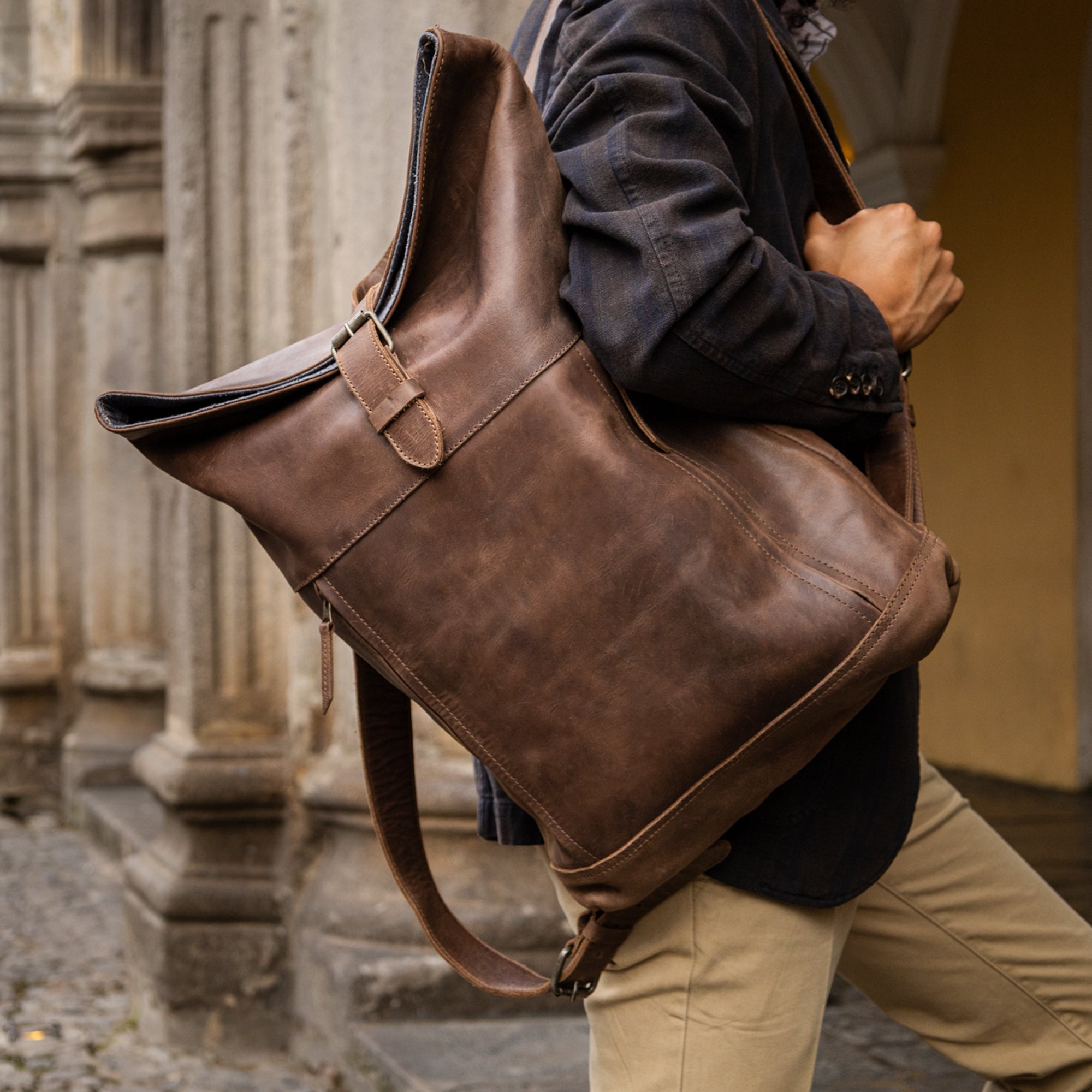 Lifestyle image of a person carrying the Roll Top Backpack by Hide & Drink, emphasizing its vintage style and practicality for travel, made from artisan-crafted full grain leather in La Antigua Guatemala.