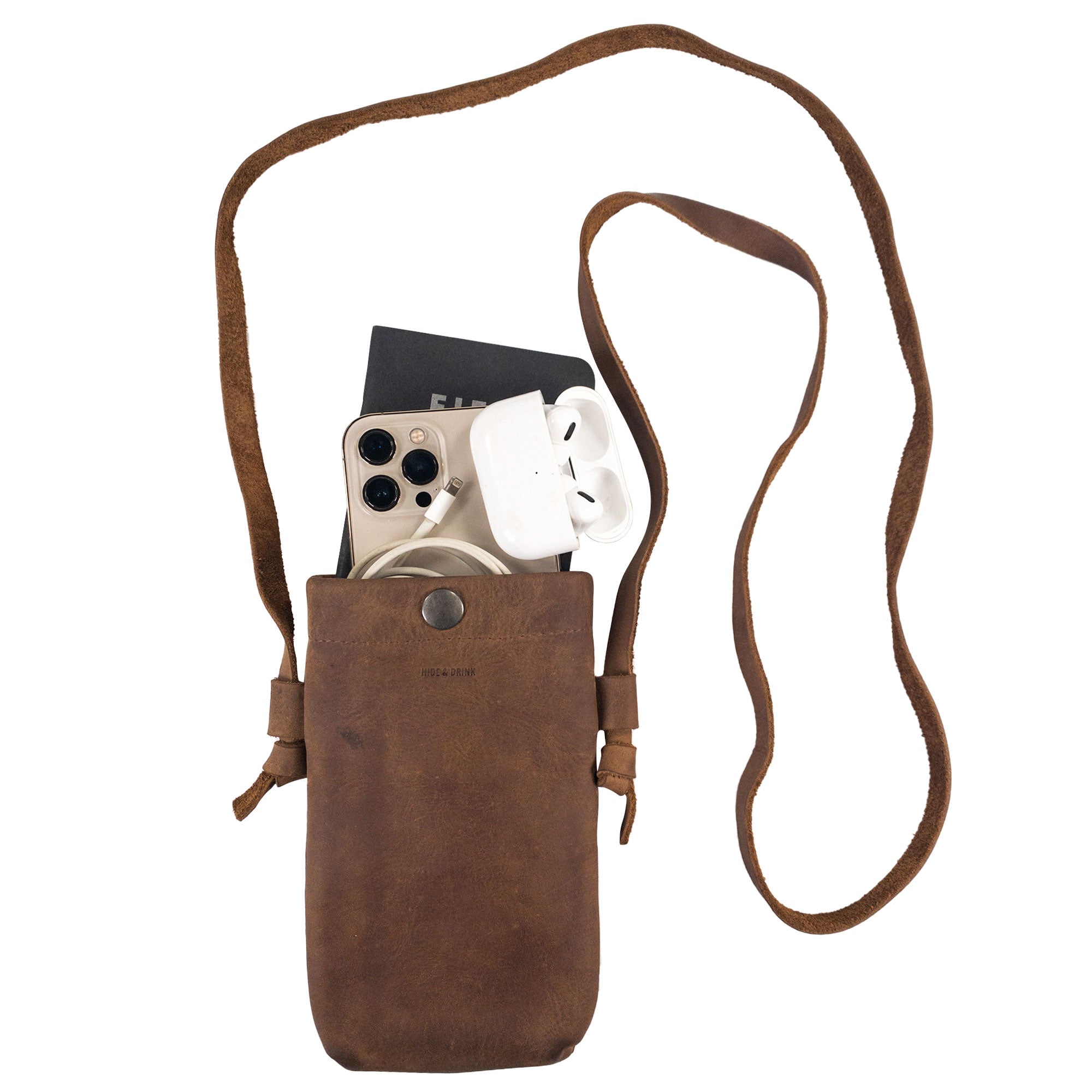 Hide & Drink Cell Phone Shoulder Bag being used to carry a smartphone and accessories, demonstrating its practical design. This full grain leather phone bag serves as a stylish travel accessory, ideal for those looking for artisan craftsmanship from La Antigua Guatemala & Oaxaca Mexico.