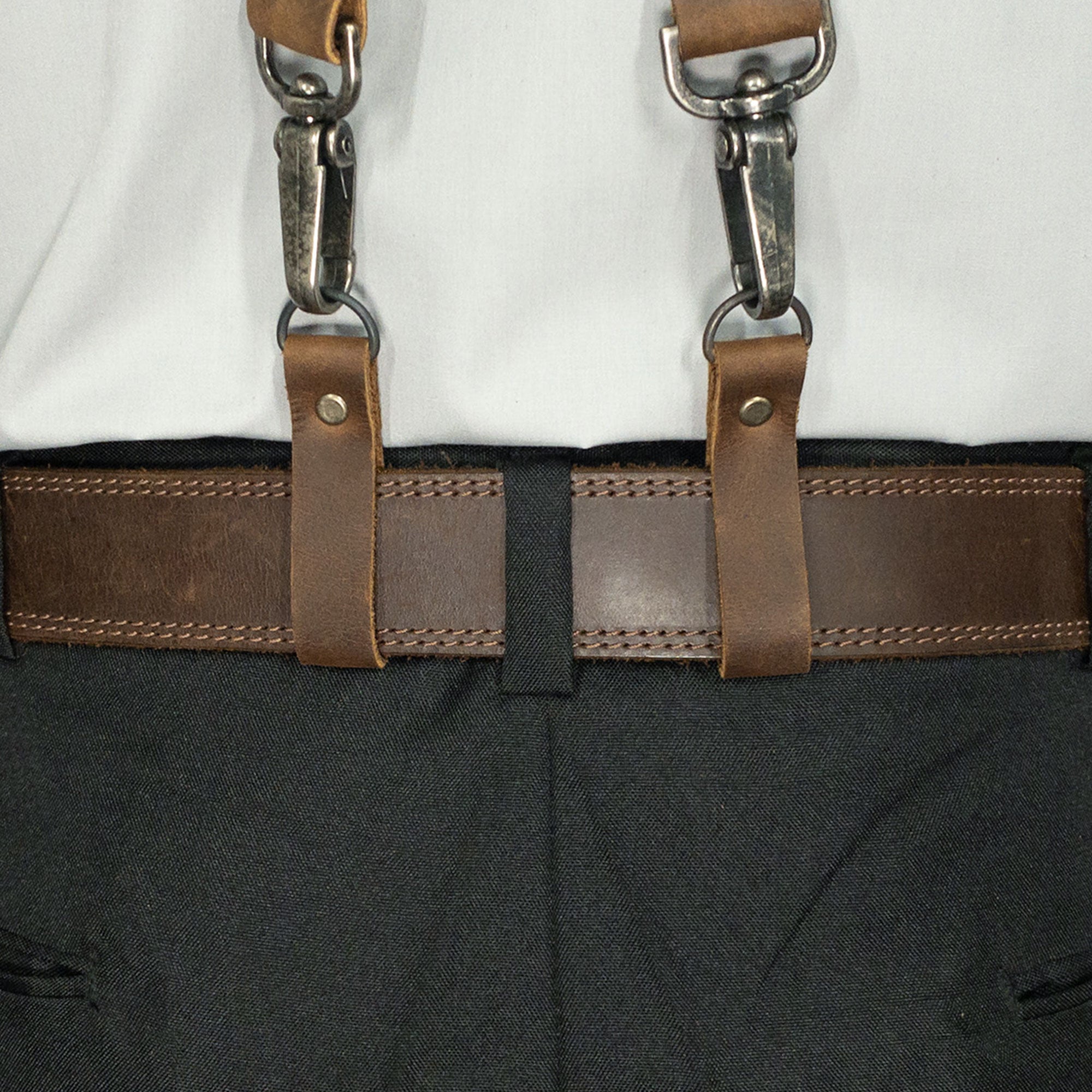 A closer look at how the Set of 4 Riveted Suspender Loop Attachments from Hide & Groom integrate with pants and suspenders, perfect for groomsmen. Crafted from full grain leather, these handmade connectors are ideal for weddings and formal gatherings, with a unique artisan touch from La Antigua Guatemala.