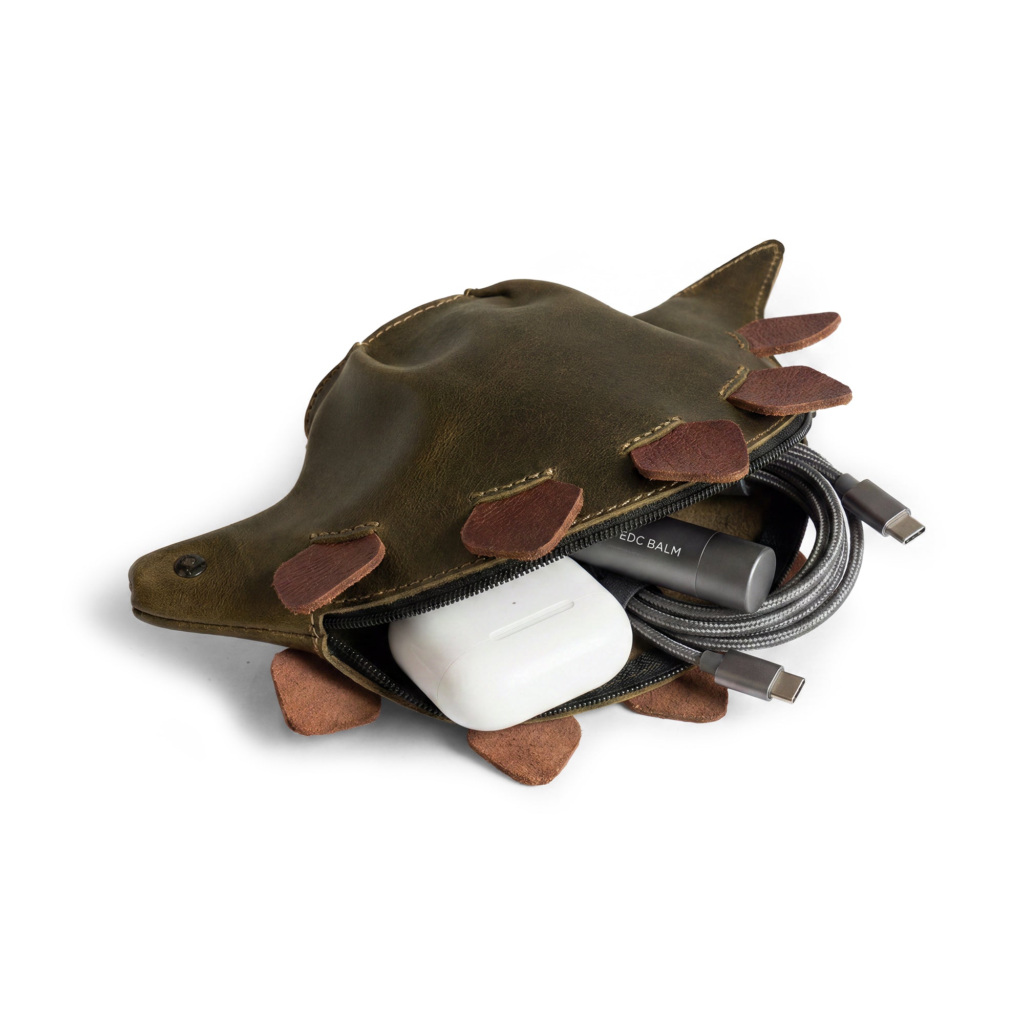 A close-up of the Leather Dinosaur Stegosaurus Pouch by Tudi Frudi, demonstrating its use as a cable organizer and zippered wallet for coins. With its playful dino-shaped exterior, this artisan-made pouch is hand sewn in La Antigua Guatemala and Oaxaca, Mexico, catering to both men and women.