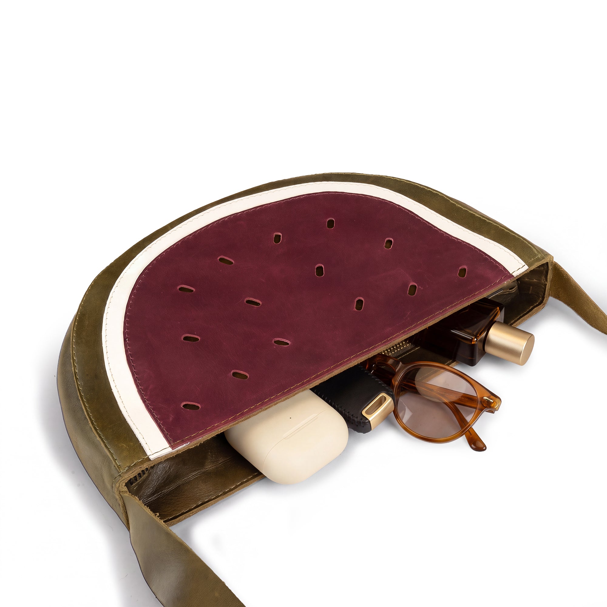 Inside view of the Watermelon-Shaped Shoulder Bag by Tudi Frudi with a phone and assorted items, demonstrating its practical design as a Crossbody Bag. This Messenger Bag is made from durable Full Grain Leather and reflects artisan craftsmanship through small batch production, hand cut, hand sewn, and fire branded techniques. Handmade in La Antigua Guatemala & Oaxaca Mexico.