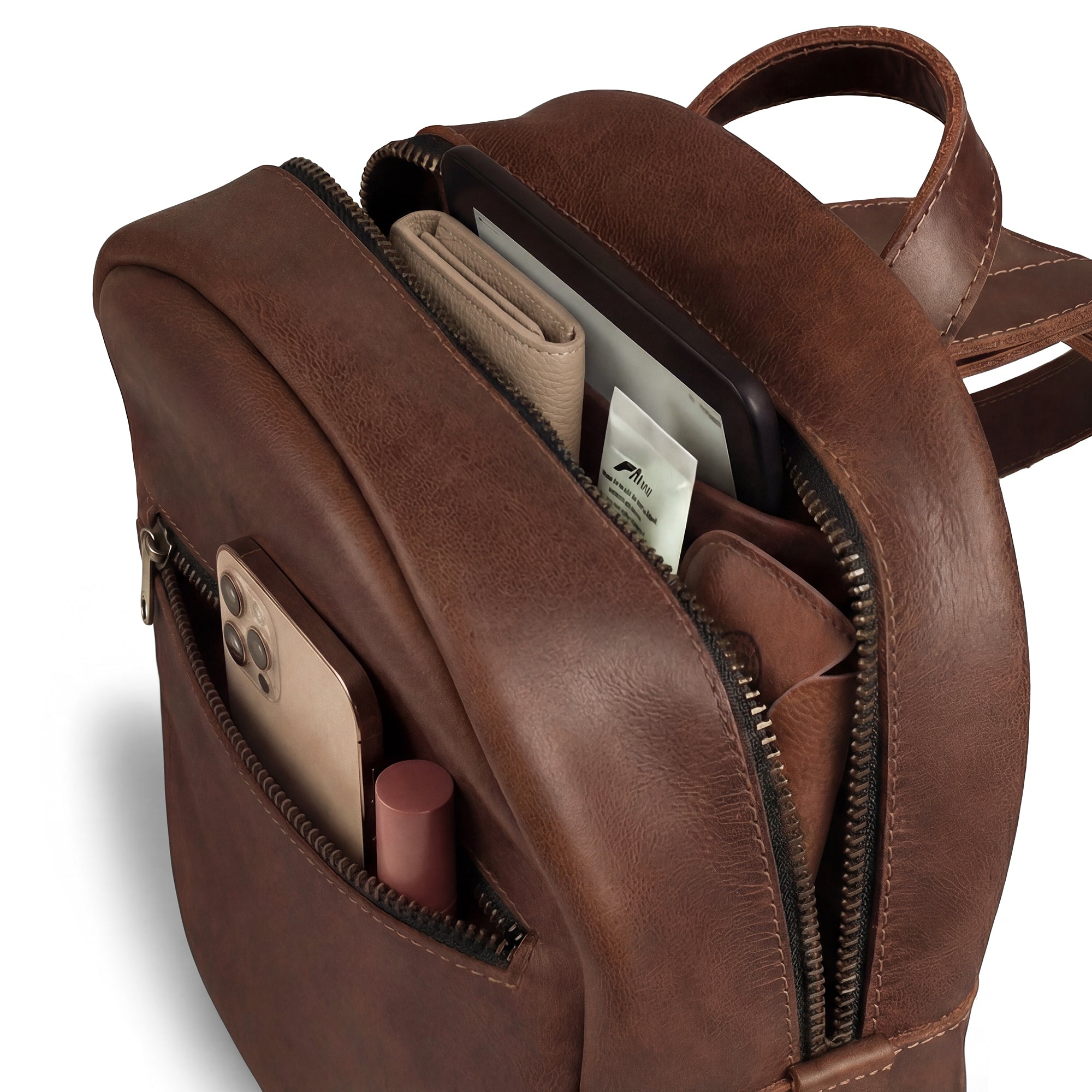 An interior view of The Holly Mini Backpack by Austin Genuine, featuring the spacious compartments filled with essentials, representing quality with tags like Full Grain Leather, StockyardX, Small Batch Production, Hand Cut, Hand Sewn, Fire Branded, Artisan, Handmade in La Antigua Guatemala & Oaxaca Mexico.
