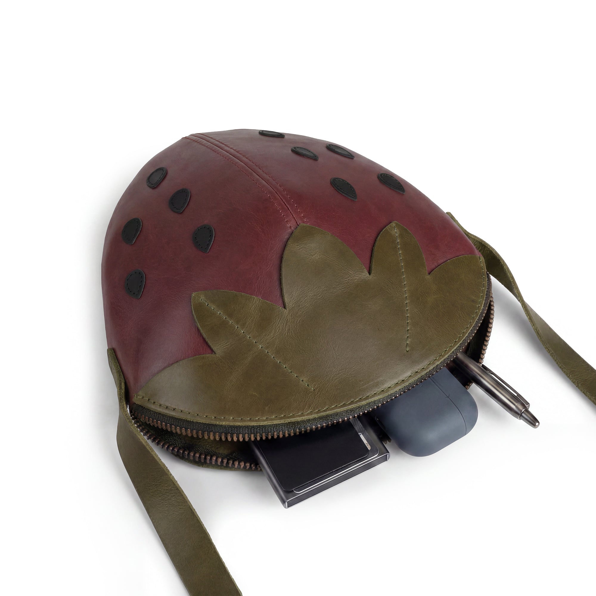 Leather Strawberry-Shaped Shoulder Bag by Tudi Frudi, showcasing the interior with a smartphone and treats. This Full Grain Leather crossbody bag combines functional design with artisanal beauty. Handmade in La Antigua Guatemala & Oaxaca Mexico, it is part of a small batch production that is hand cut and hand sewn.