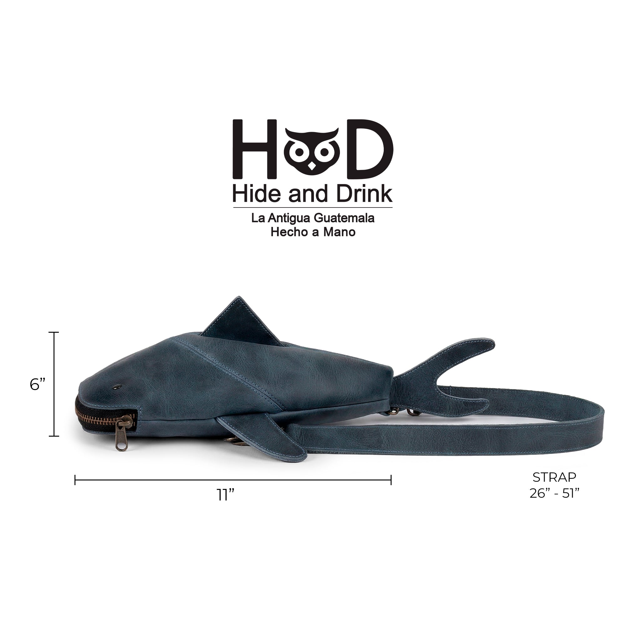 The Leather Shark Crossbody Bag by Hide & Drink, displayed with key dimensions and features. This unique shark-shaped design is made of full grain leather and boasts an adjustable strap for versatile wear as a messenger bag or shoulder bag. Handmade in La Antigua Guatemala & Oaxaca Mexico, this Leather Shark-Shaped Sling Bag is perfect for those seeking a stylish yet practical accessory.