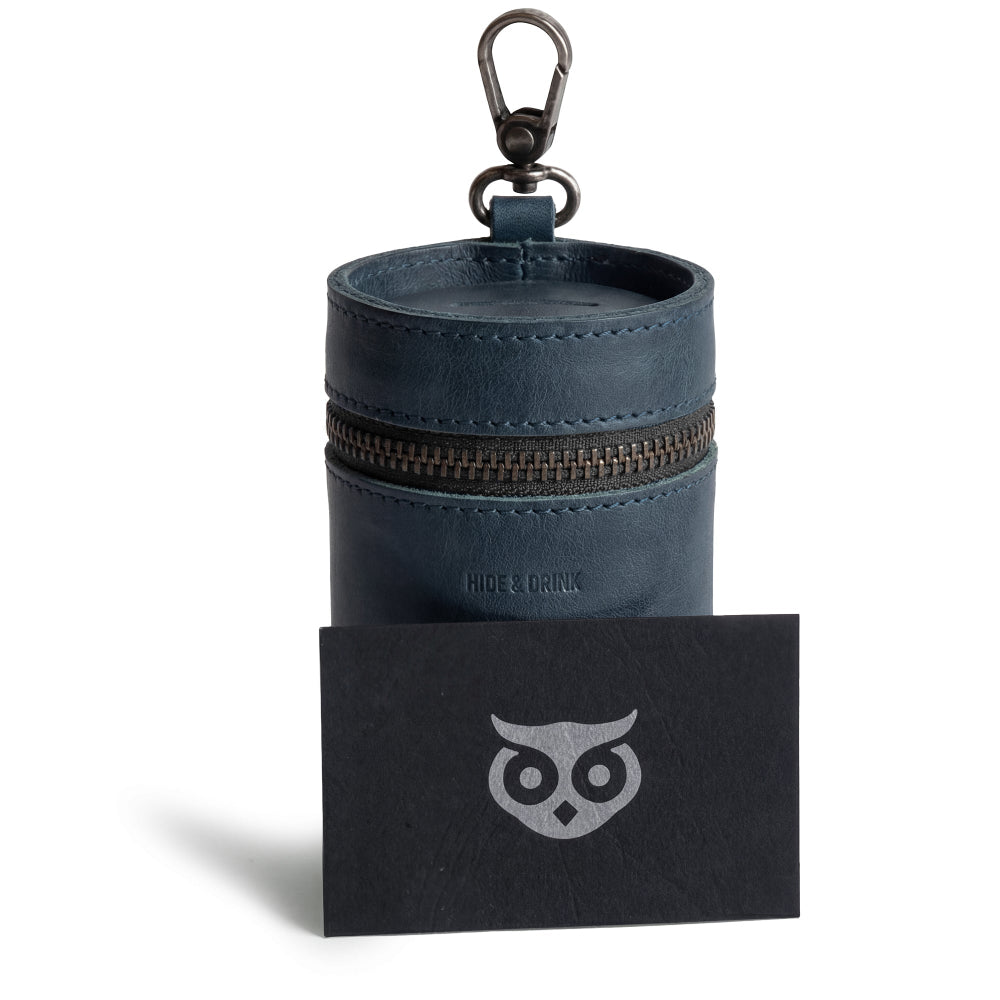 Hide & Drink Bucket Coin Release presented alongside a card. This unique money box, fashioned as a piggy bank bucket and zippered pouch, is made of full grain leather, showcasing artisan craftsmanship straight from La Antigua Guatemala & Oaxaca Mexico.