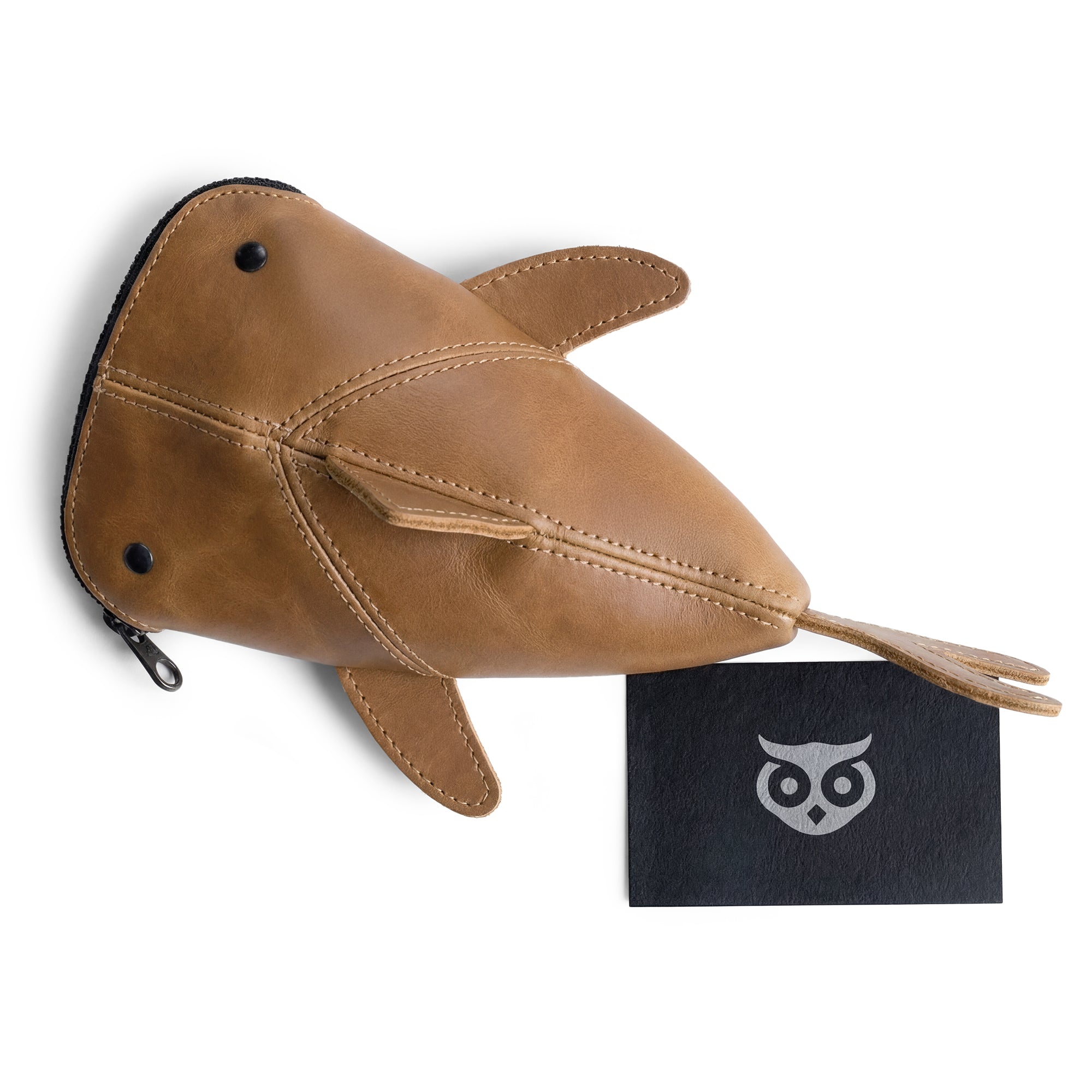 Overhead view of the Hide & Drink Leather Shark Pouch next to a branded card. This artistic zippered pouch serves multiple purposes, from being a wallet to a stuffed animal storage solution. Made from full grain leather, it represents small batch production, hand cut, and hand sewn craftsmanship by artisans in La Antigua Guatemala & Oaxaca Mexico.