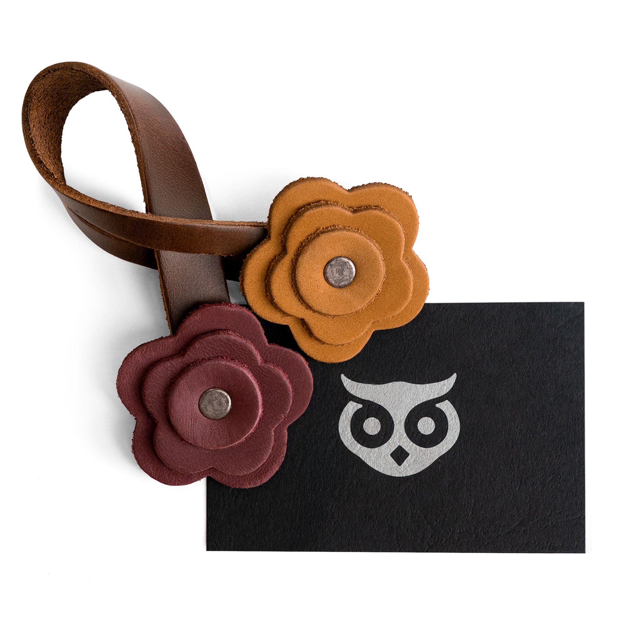 The Rose Bag Ornament by Hide & Drink elegantly laid out with a card, showcasing its Full Grain Leather craftsmanship and flower-shaped design. This accessory is a perfect charm for bags and totes.