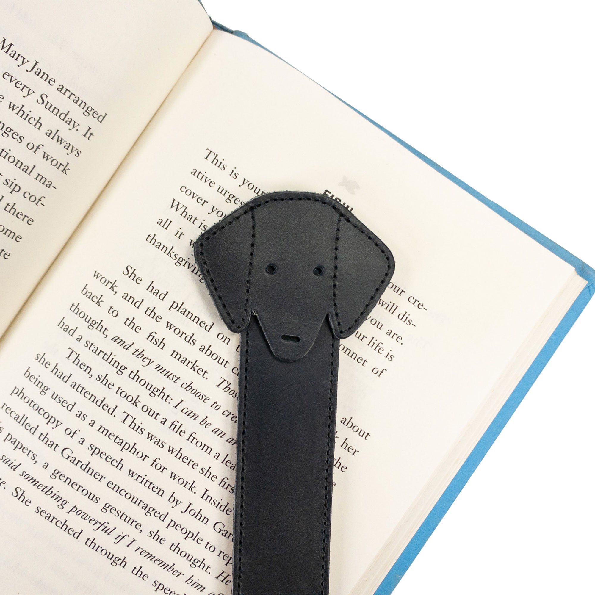 Close-up of Hide & Drink's black Dog Bookmark resting on a book, highlighting its Full Grain Leather craftsmanship. This handmade item is a testament to small batch production and fire branding, crafted in La Antigua Guatemala & Oaxaca Mexico.