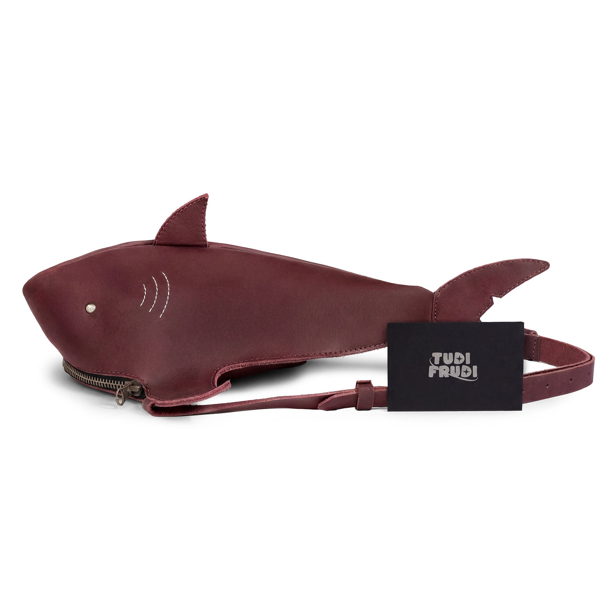 Illustration of the Shark-Shaped Shoulder Bag by Tudi Frudi, positioned with its tag. Made in La Antigua Guatemala, this bag showcases Full Grain Leather craftsmanship, designed for versatility as a crossbody or messenger bag, representing artisan excellence and small batch production.