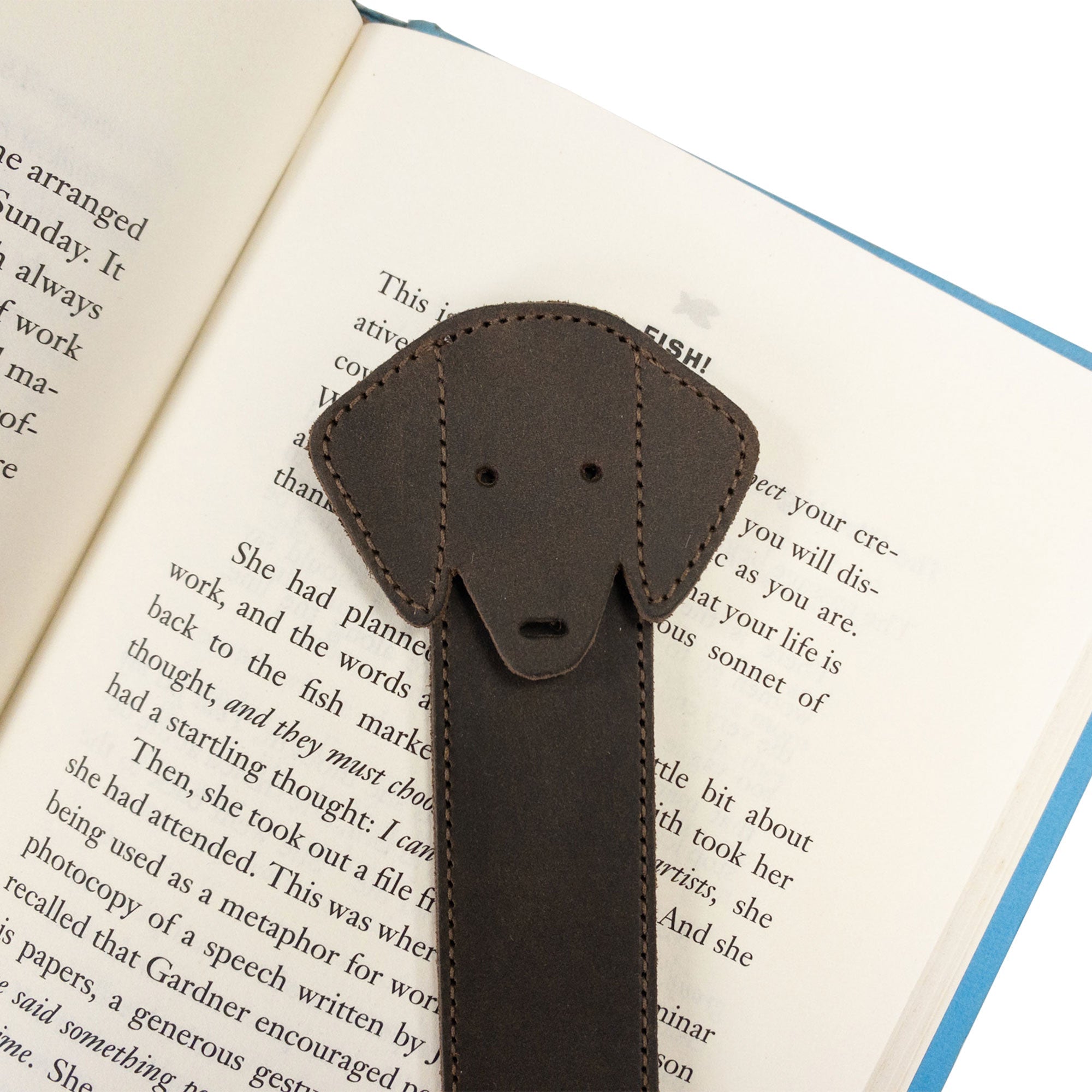 Hide & Drink's Dog Bookmark nestled on a book page, made from Full Grain Leather. This artisan, handmade bookmark features thoughtful details of small batch production and fire branding from La Antigua Guatemala & Oaxaca Mexico.