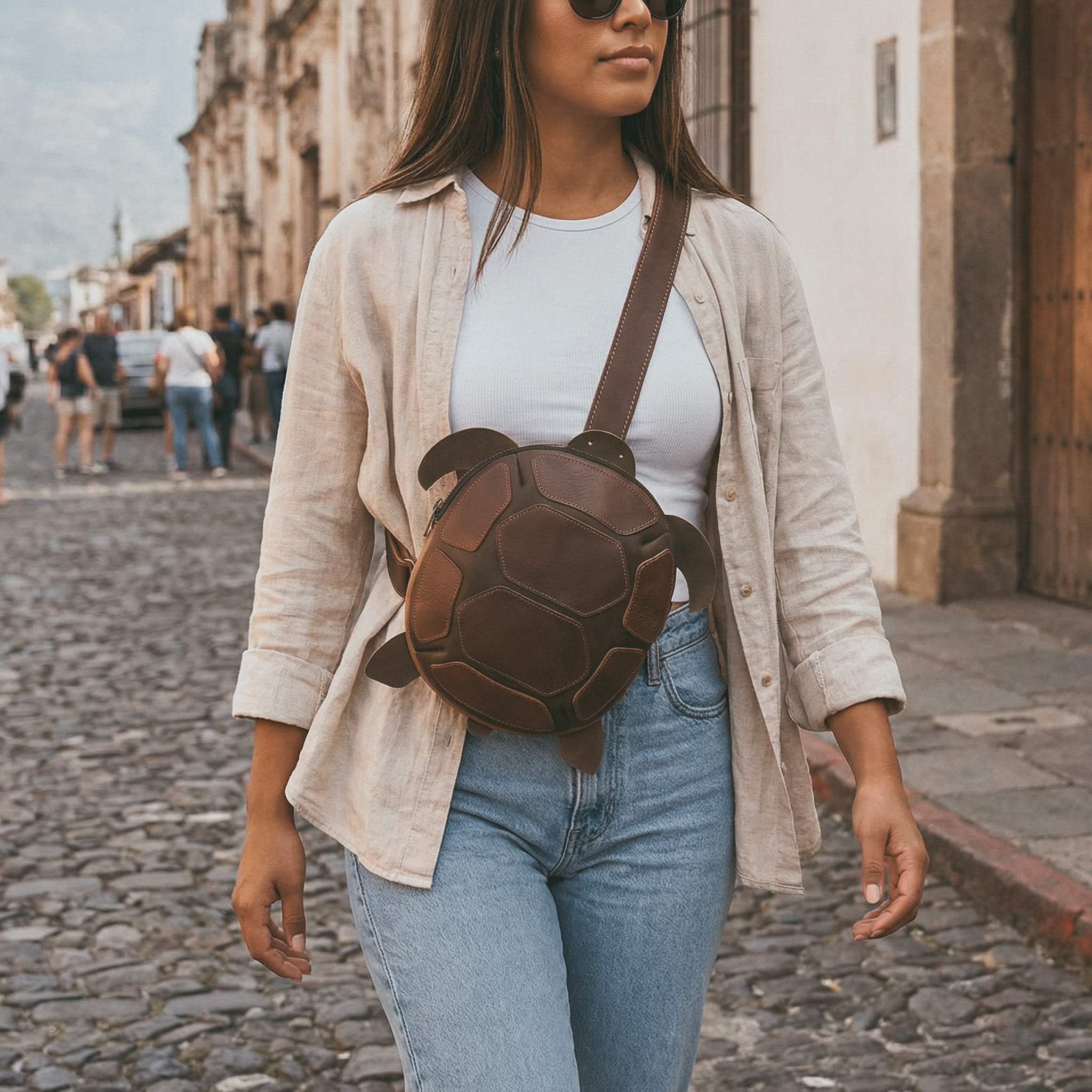 Lifestyle image featuring the Leather Turtle-Shaped Crossbody Bag by Hide & Play being worn casually. This turtle-shaped messenger bag is crafted from full grain leather, making it a stylish accessory for travel. Handmade in La Antigua Guatemala & Oaxaca Mexico, this bag combines functionality with small batch artisan craftsmanship.