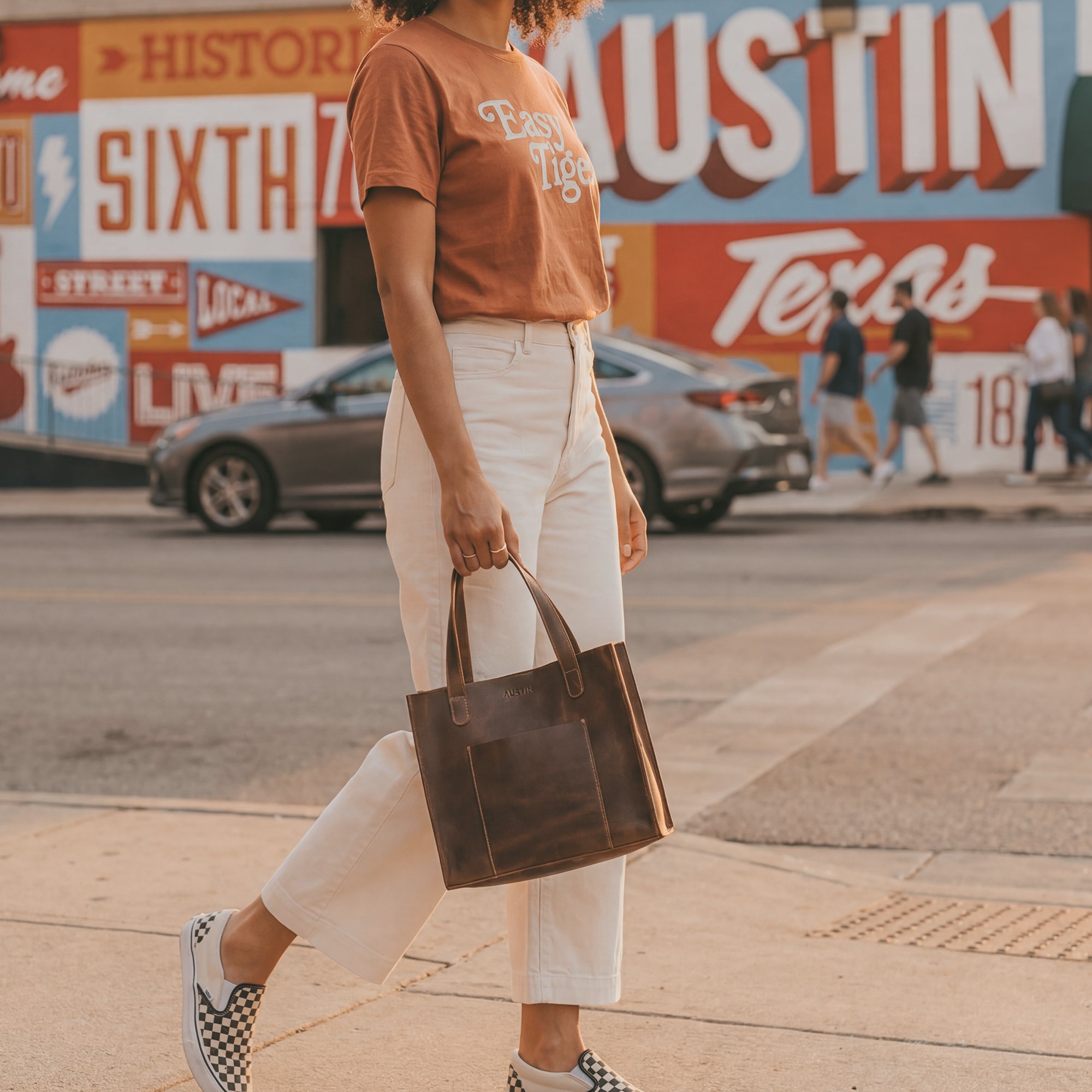 A person stylishly carrying The Springdale Crossbody Tote by Austin Genuine, featuring its full grain leather design. This artisan tote, made through small batch production in La Antigua Guatemala & Oaxaca Mexico, highlights unique craftsmanship.