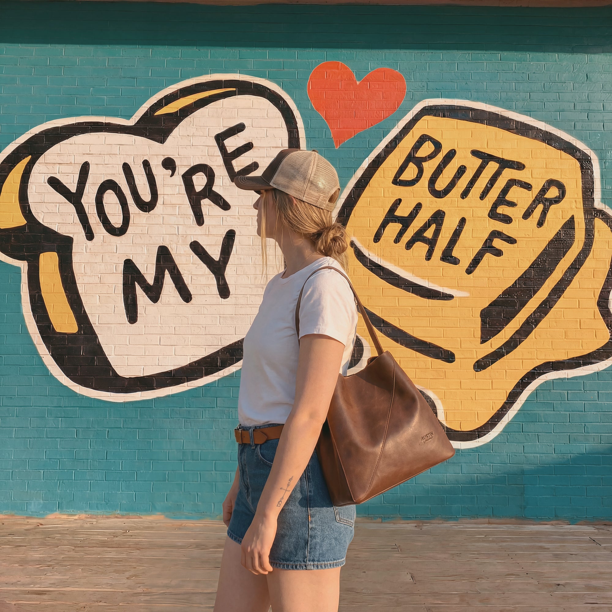 Lifestyle shot of The Pemberton Shoulder Bag by Austin Genuine, worn casually against a vibrant mural, showcasing the stylish blend of full grain leather and artisanal craftsmanship.