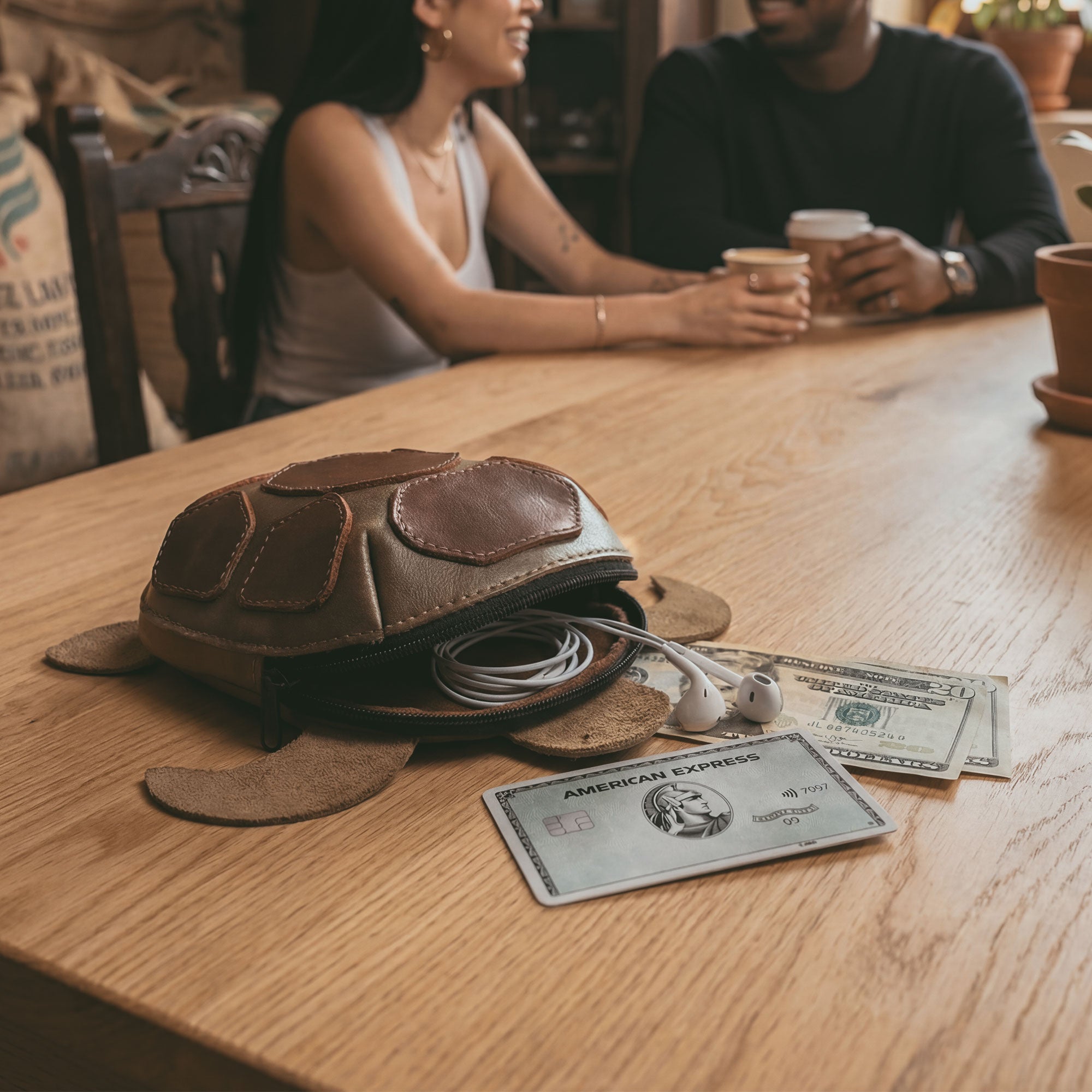 Hide & Play Leather Turtle Pouch in use on a café table, showing the hand cut and hand sewn full grain leather turtle-shaped coin pouch change bag and tortoise-shaped leather coin purse with purses & pouches for cash and a zippered cable case—small charger cable holder for a tiny travel carrier; small batch production, fire branded artisan handmade in La Antigua Guatemala & Oaxaca Mexico (StockyardX).