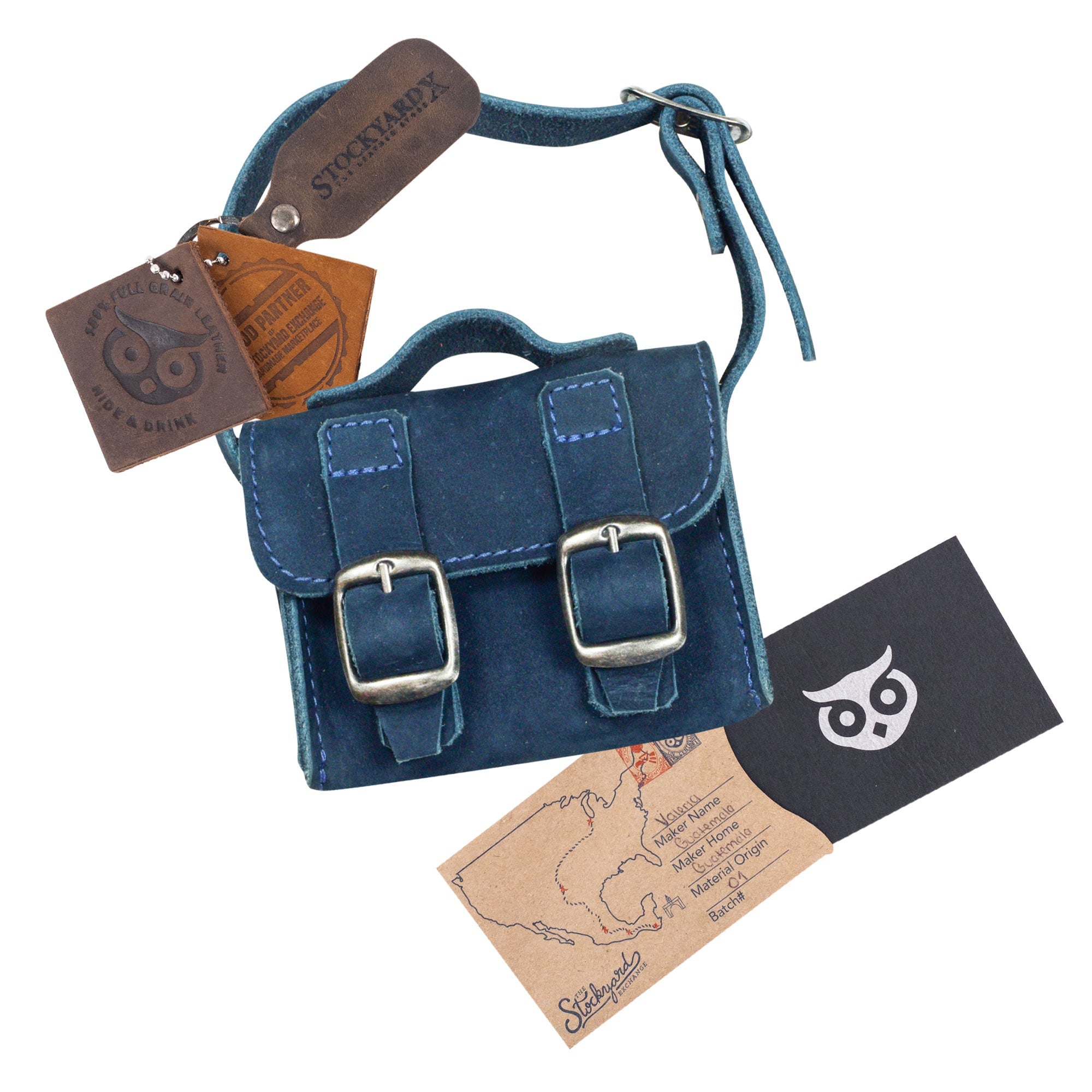 The navy Tiny Messenger Bag by Hide & Drink, accompanied by its signature tags. This Mini Messenger Bag Charm, crafted from premium Full Grain Leather, is ideal as a keychain or handbag accessory, reflecting fine artisan work made in La Antigua Guatemala.