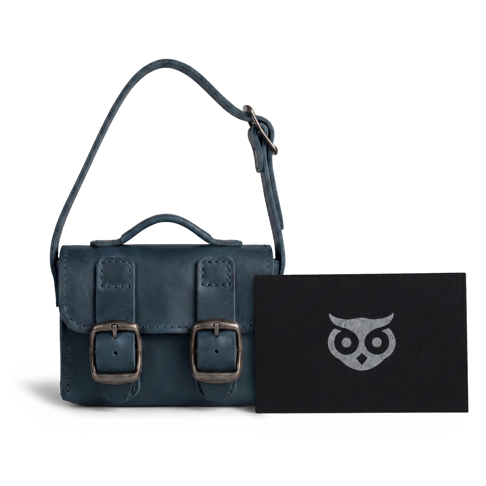 The deep blue Tiny Messenger Bag by Hide & Drink, presented with its tags. This artisan Mini Messenger Bag Charm in Full Grain Leather serves as an excellent keychain or handbag accessory, handcrafted in La Antigua Guatemala.